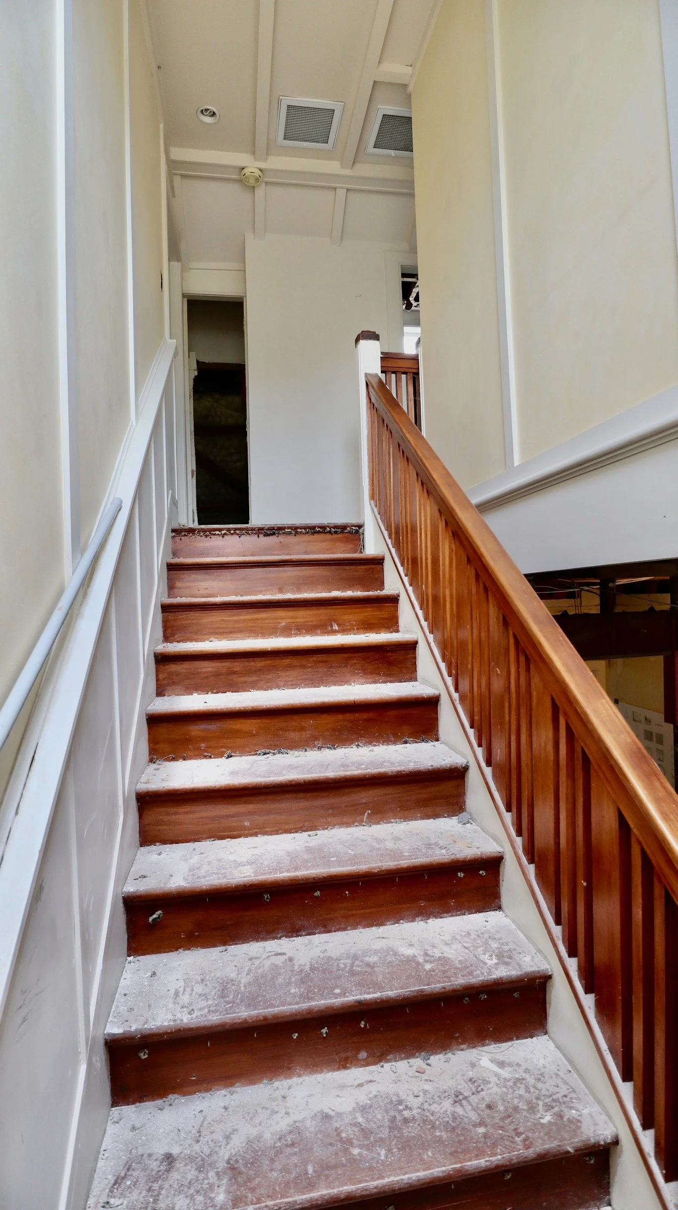 Wooden staircase with dusty steps and partial wall paneling, leading upward in a house interior.