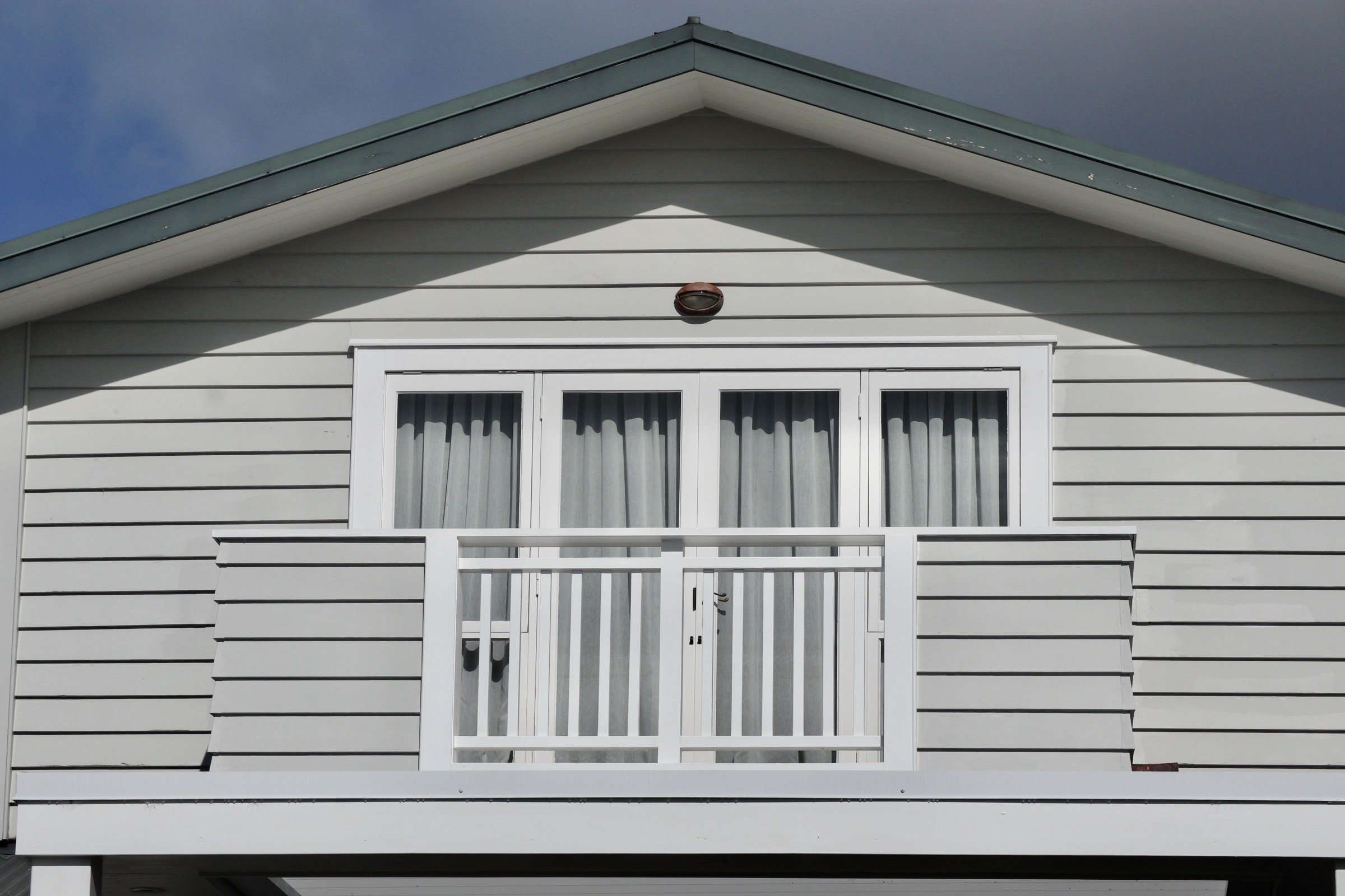 Front view of a house with white siding, a gable roof, a balcony with a white railing, and a sliding glass door with curtains.