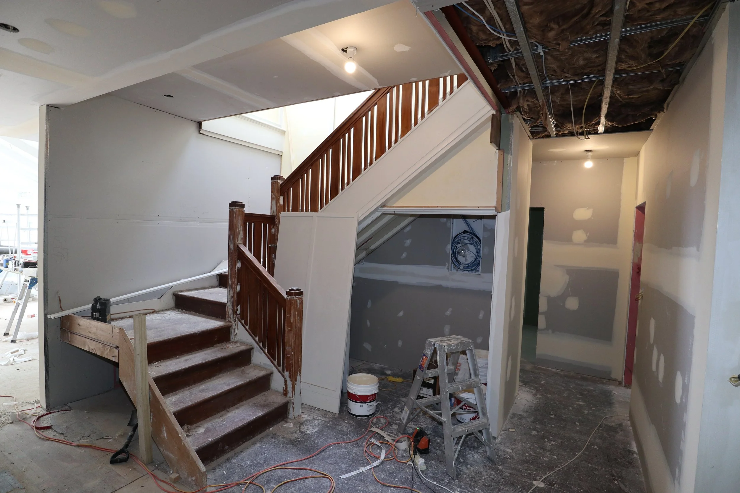 Interior of a house under renovation with stairs, partially constructed walls, and exposed ceiling wiring.