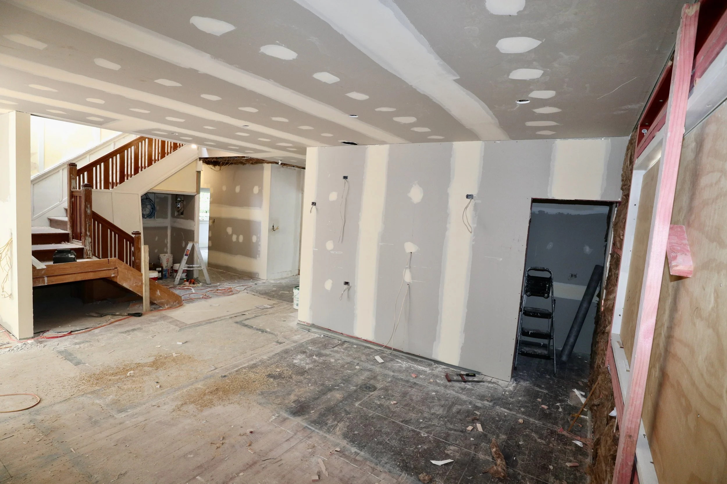 Interior of a house under renovation with drywall installation, unfinished walls, and construction tools on the floor.