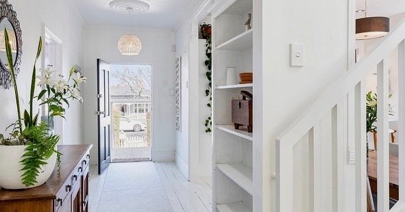Bright entryway with white walls, open front door, and built-in white shelving unit on the right, decorated with plants and decorative items.