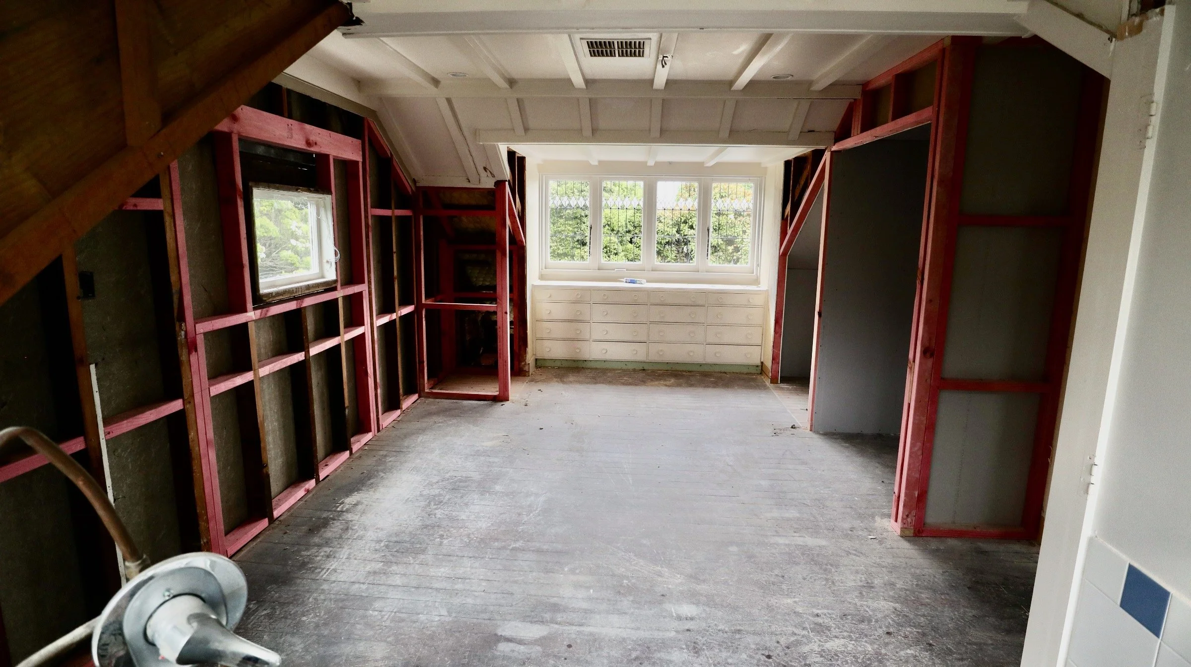 Interior of a room under construction with exposed framing, a window at the end, and a built-in white dresser below the window.