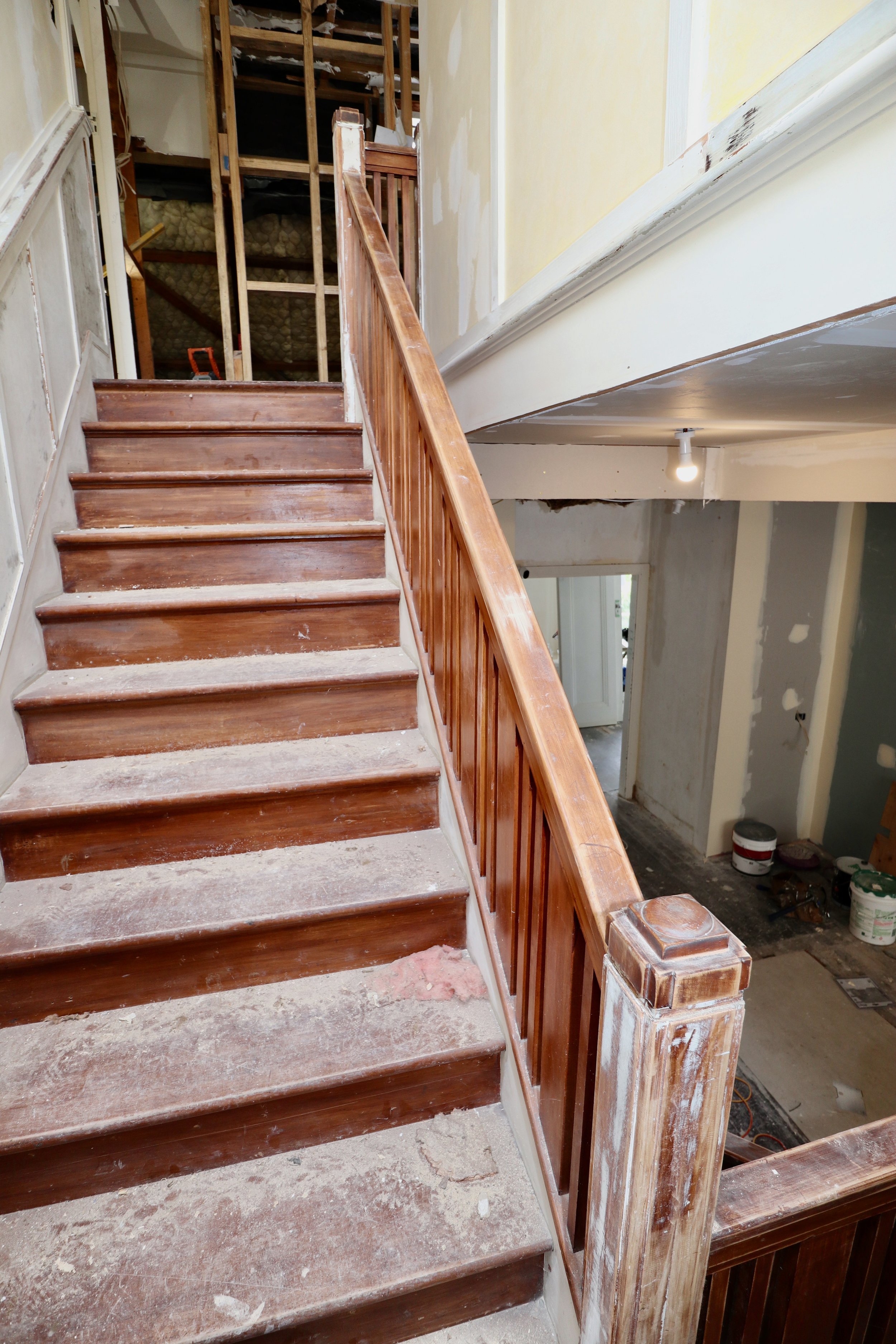 Wooden staircase undergoing renovation inside a house, with unfinished walls and construction tools.