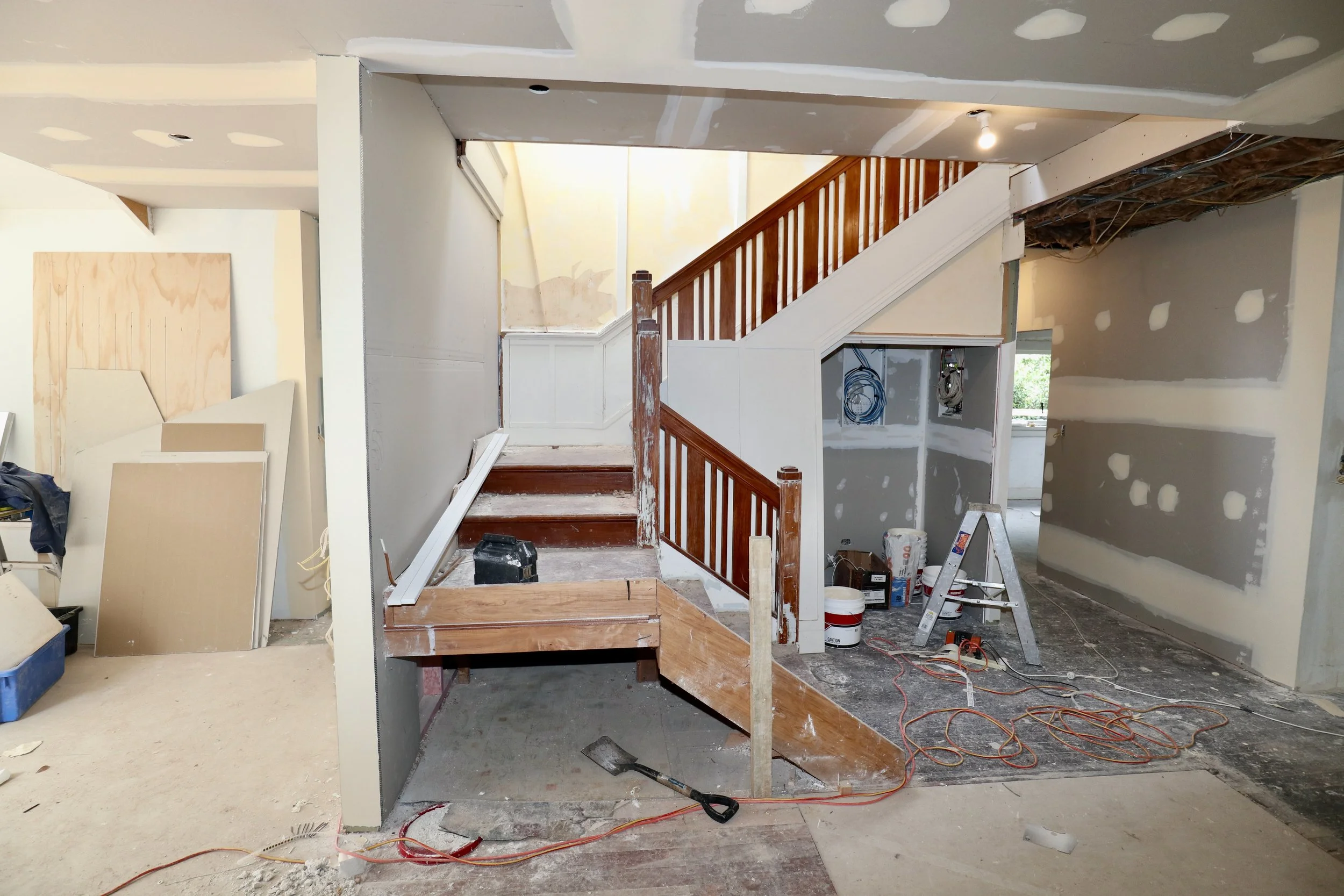 Interior of a house under renovation with stairs, drywall, construction tools, and materials.