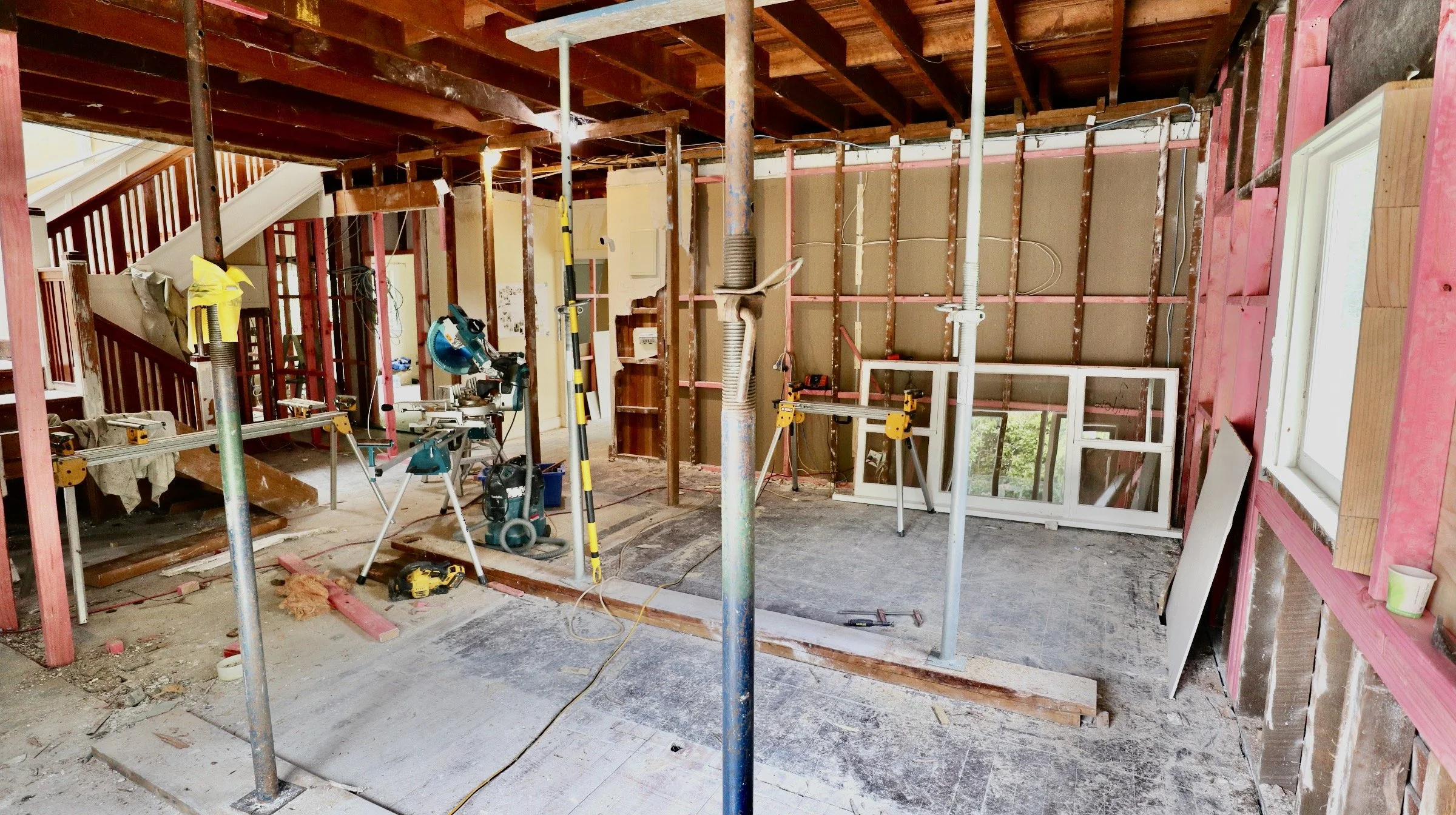 Interior of a house under renovation with construction tools, scaffolding, and partially installed walls and windows.