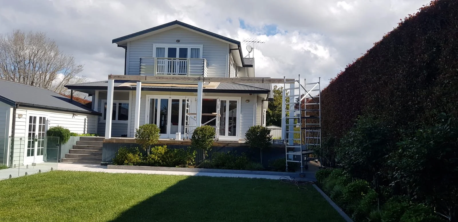 Two-story white house with a balcony, construction scaffolding on the back deck, and a neatly maintained green lawn.