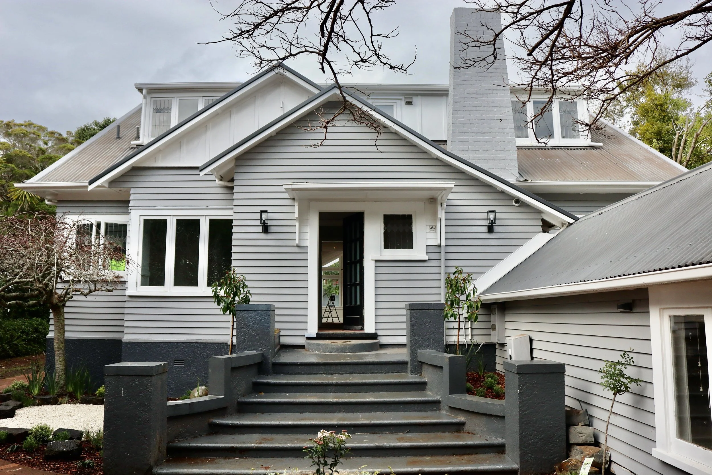 Front view of a large, white, two-story house with gray siding, steps leading up to the front door, and some trees around it.