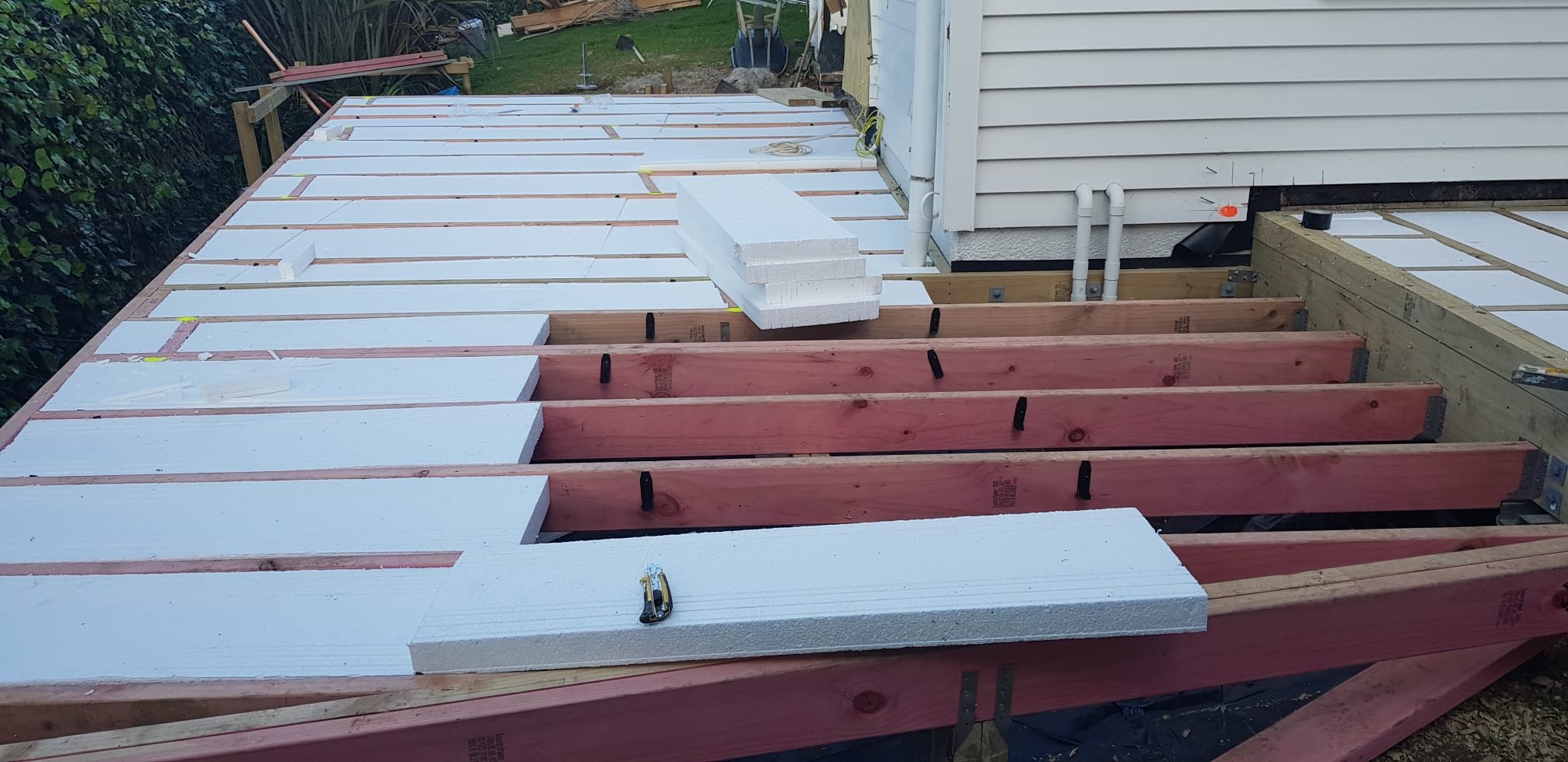 Construction site showing a partially built deck with wooden beams and white foam insulation panels installed.