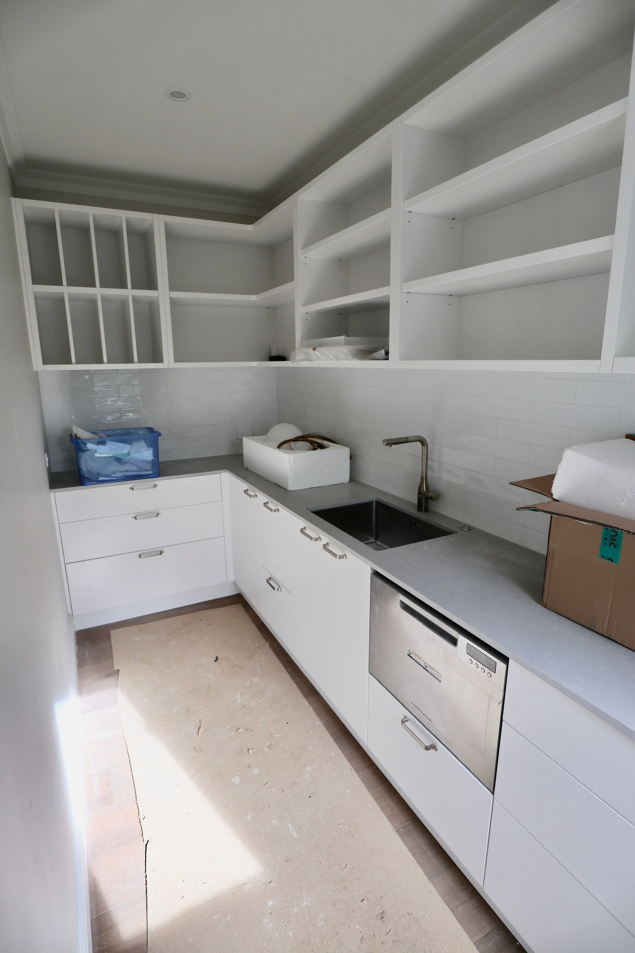 A kitchen under construction with white cabinets, open shelving, a gray countertop, and a black sink.