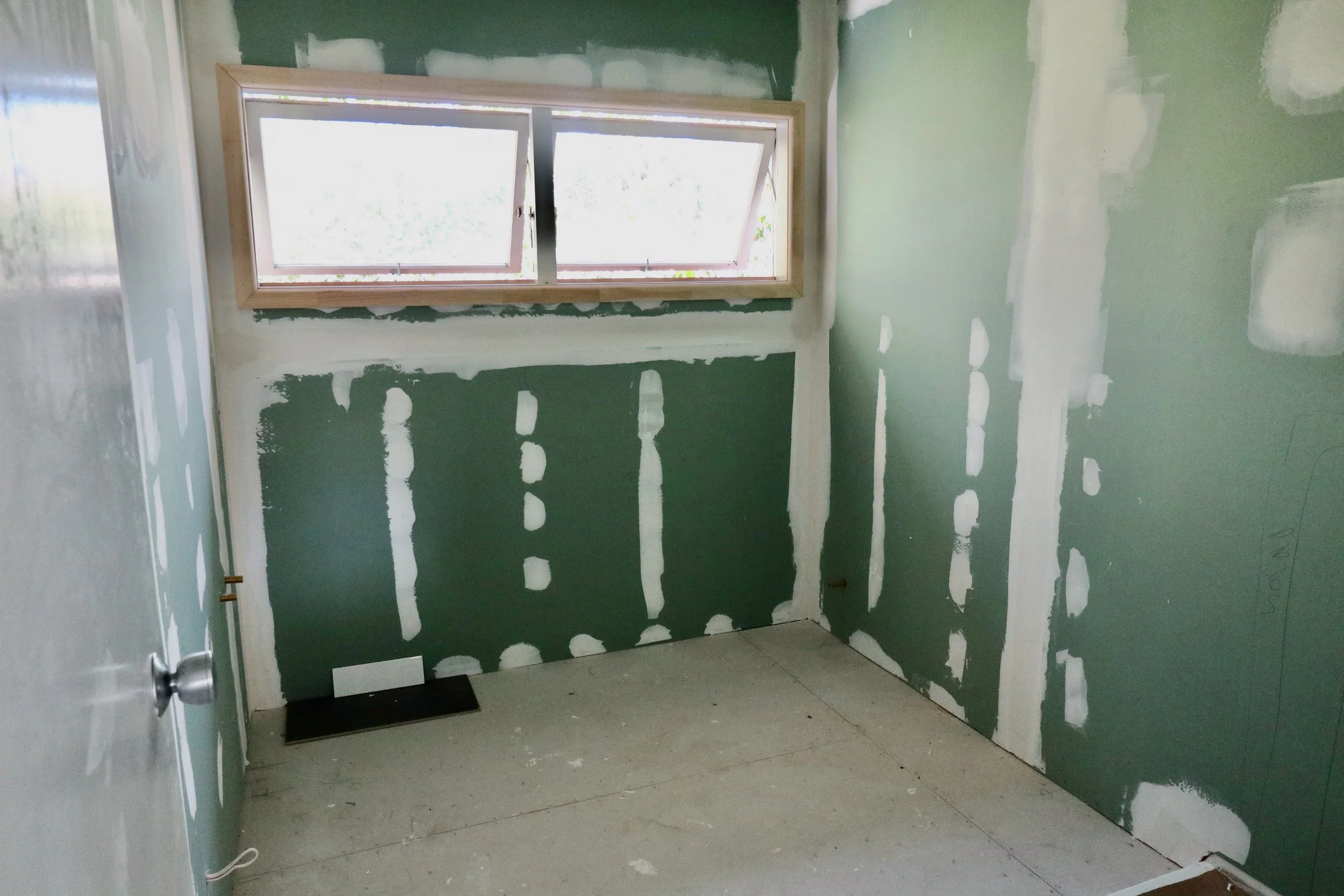 Empty room with green drywall, window, and unfinished walls.