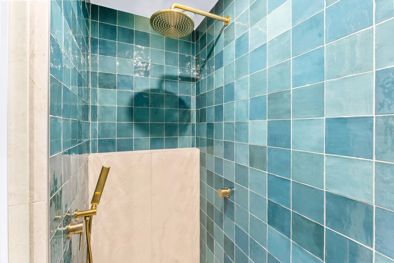 Shower area with blue tiled walls, a large round showerhead, golden fixtures, and a handheld shower wand.
