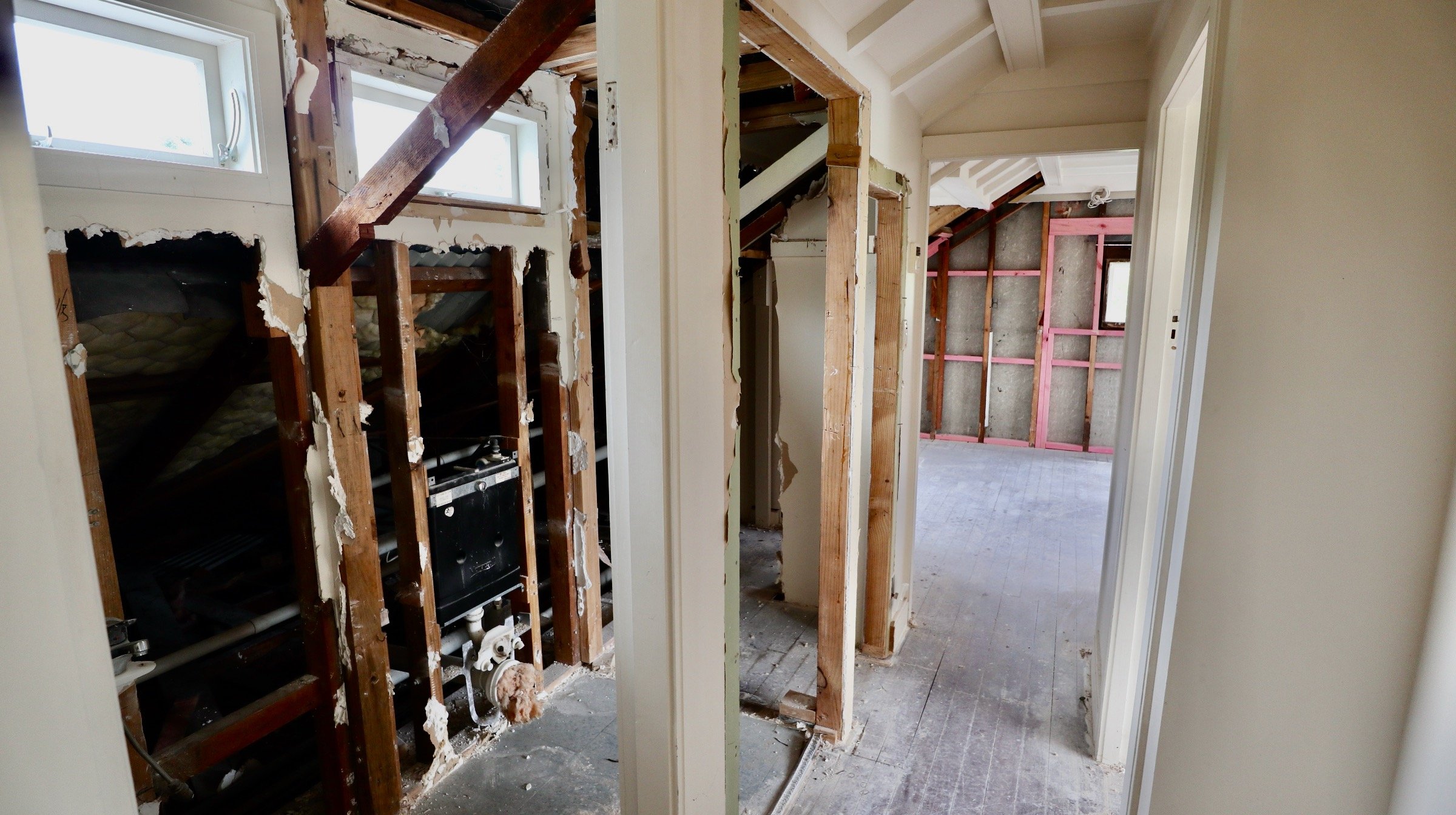 Interior of a house under renovation with exposed wooden framing, electrical wiring, insulation, and open walls, showing rooms in progress.