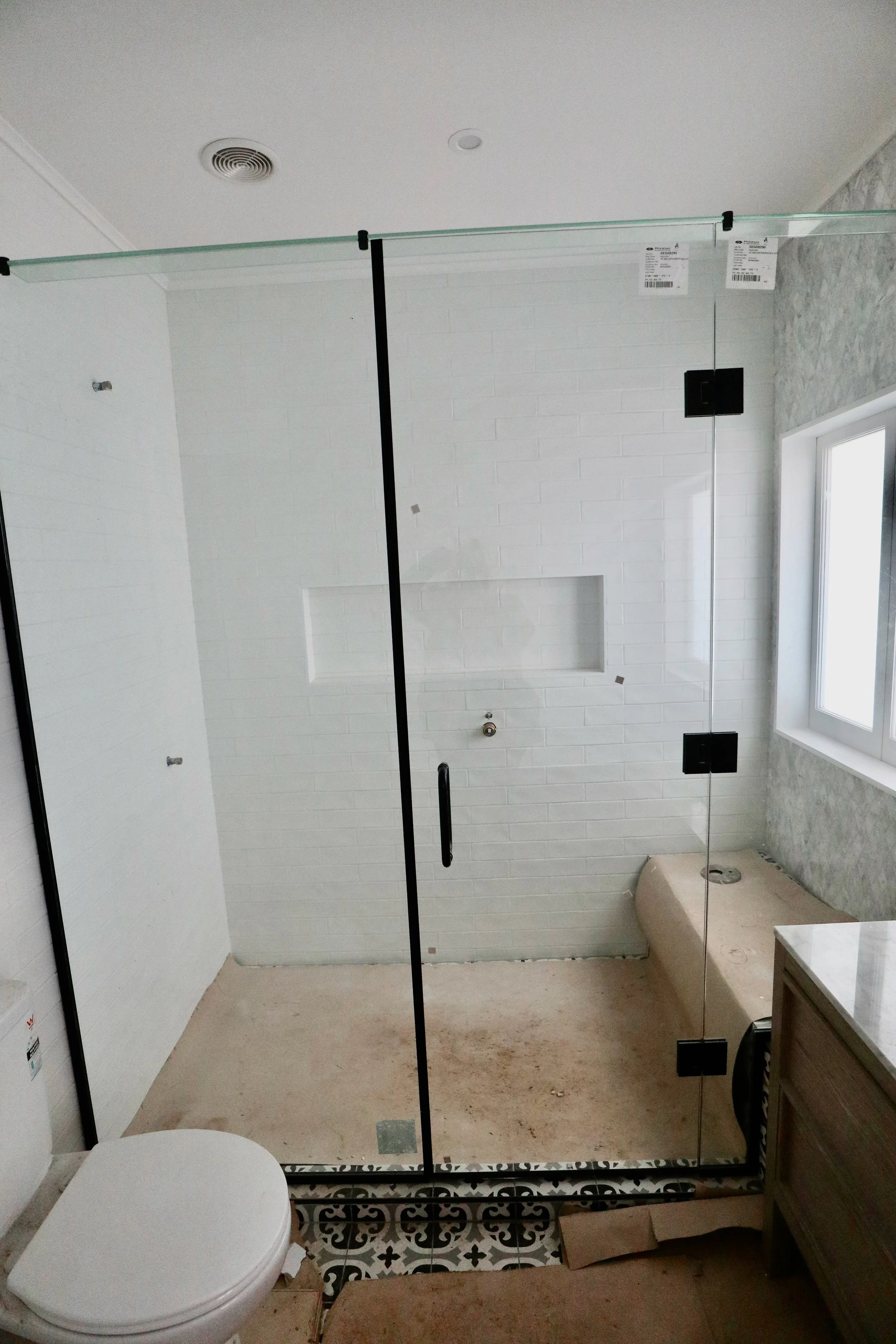 Bathroom under renovation with a glass shower enclosure, a toilet, and a window.