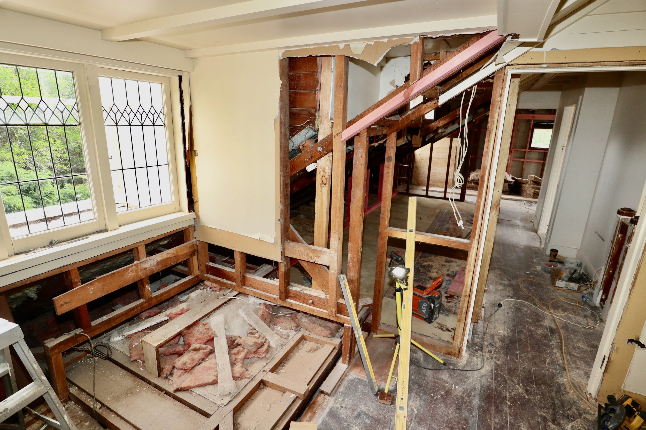 Interior of a house under renovation with exposed wooden framing, construction tools, and debris.