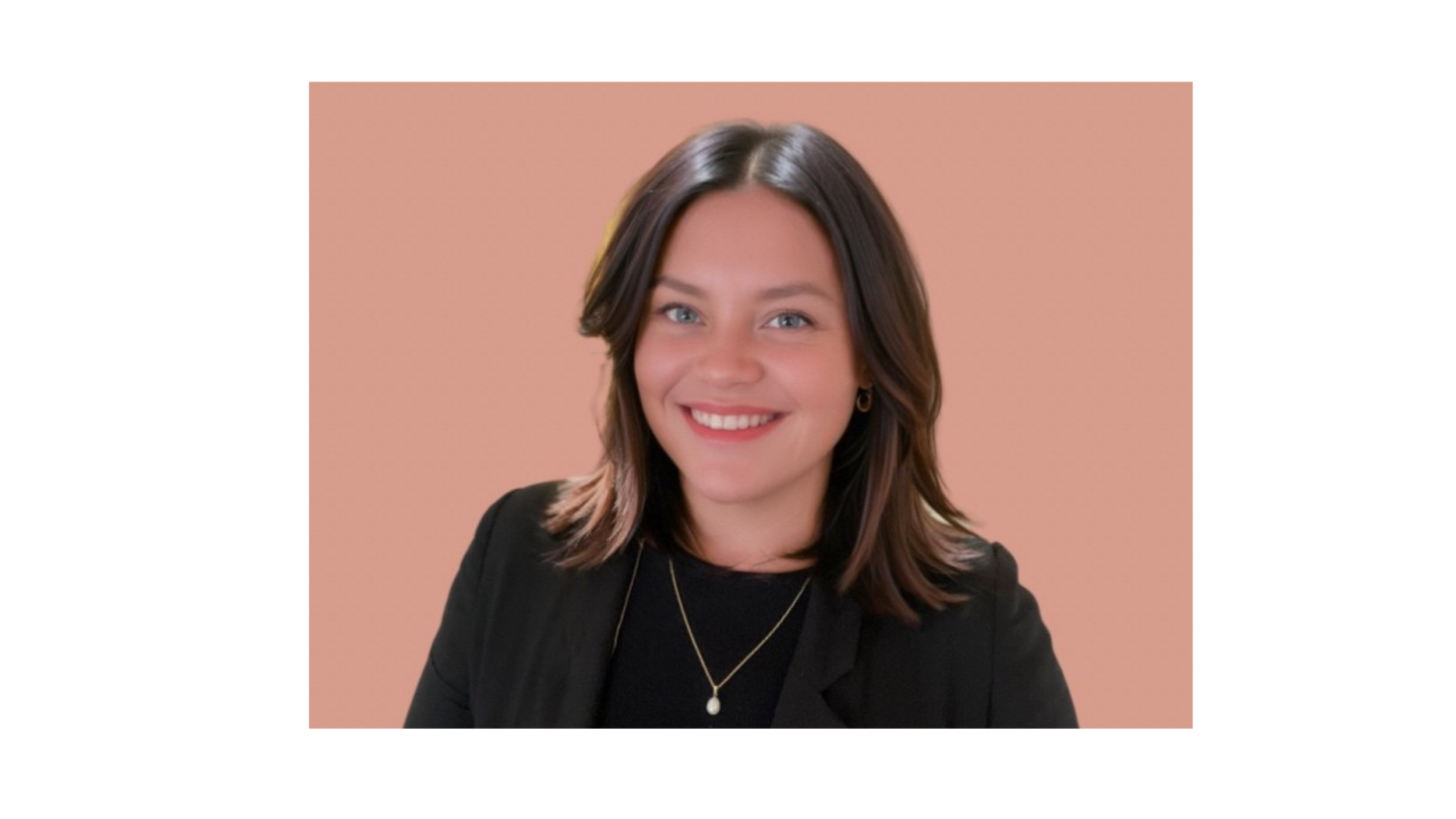 A woman with shoulder-length dark brown hair, smiling, wearing a black blazer, black top, gold necklace with a pearl pendant, and small gold hoop earrings, against a soft pink background.