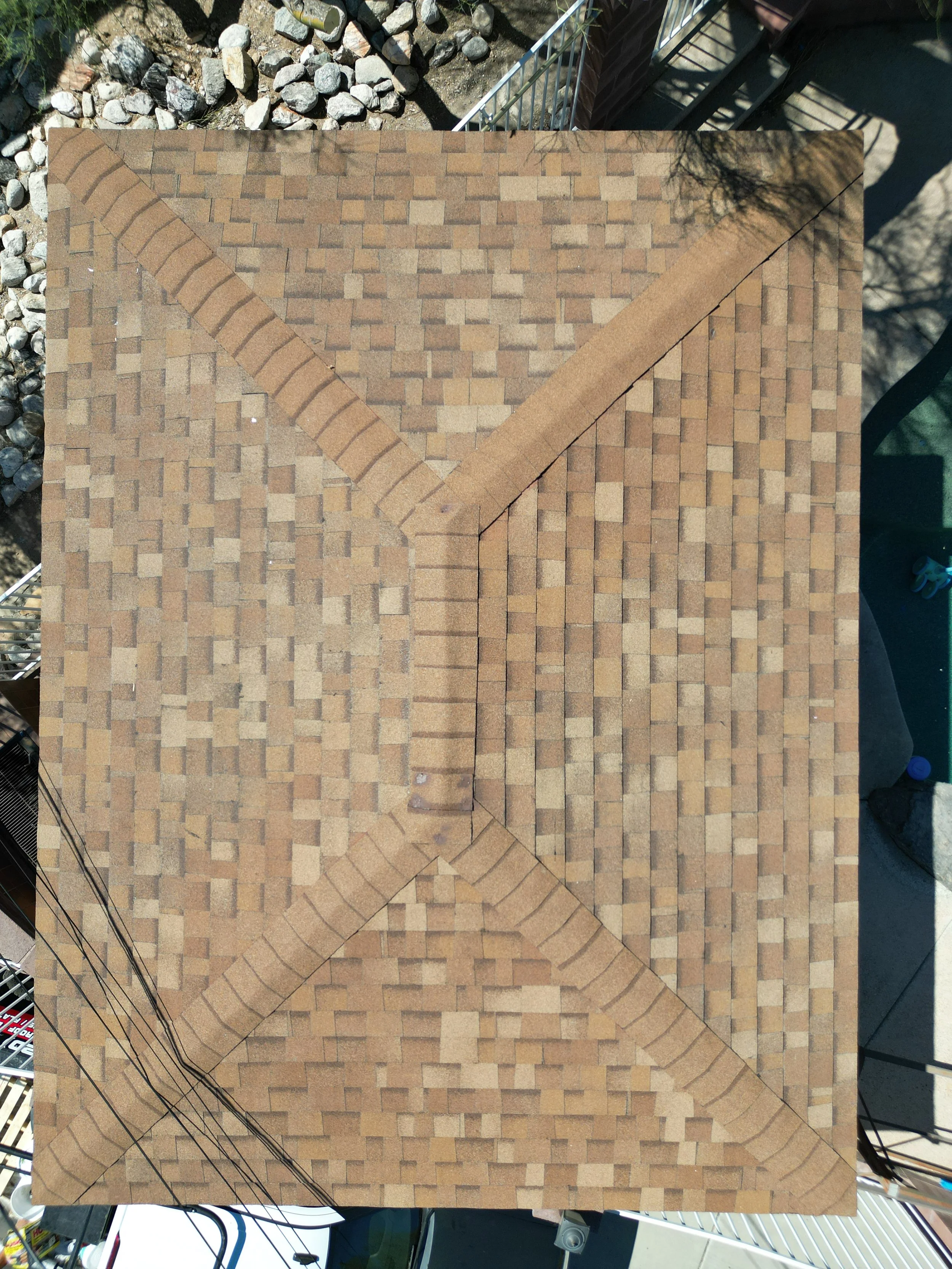 An aerial view of a rooftop with a shingle roof pattern, divided into four sections by diagonal lines of darker shingles.