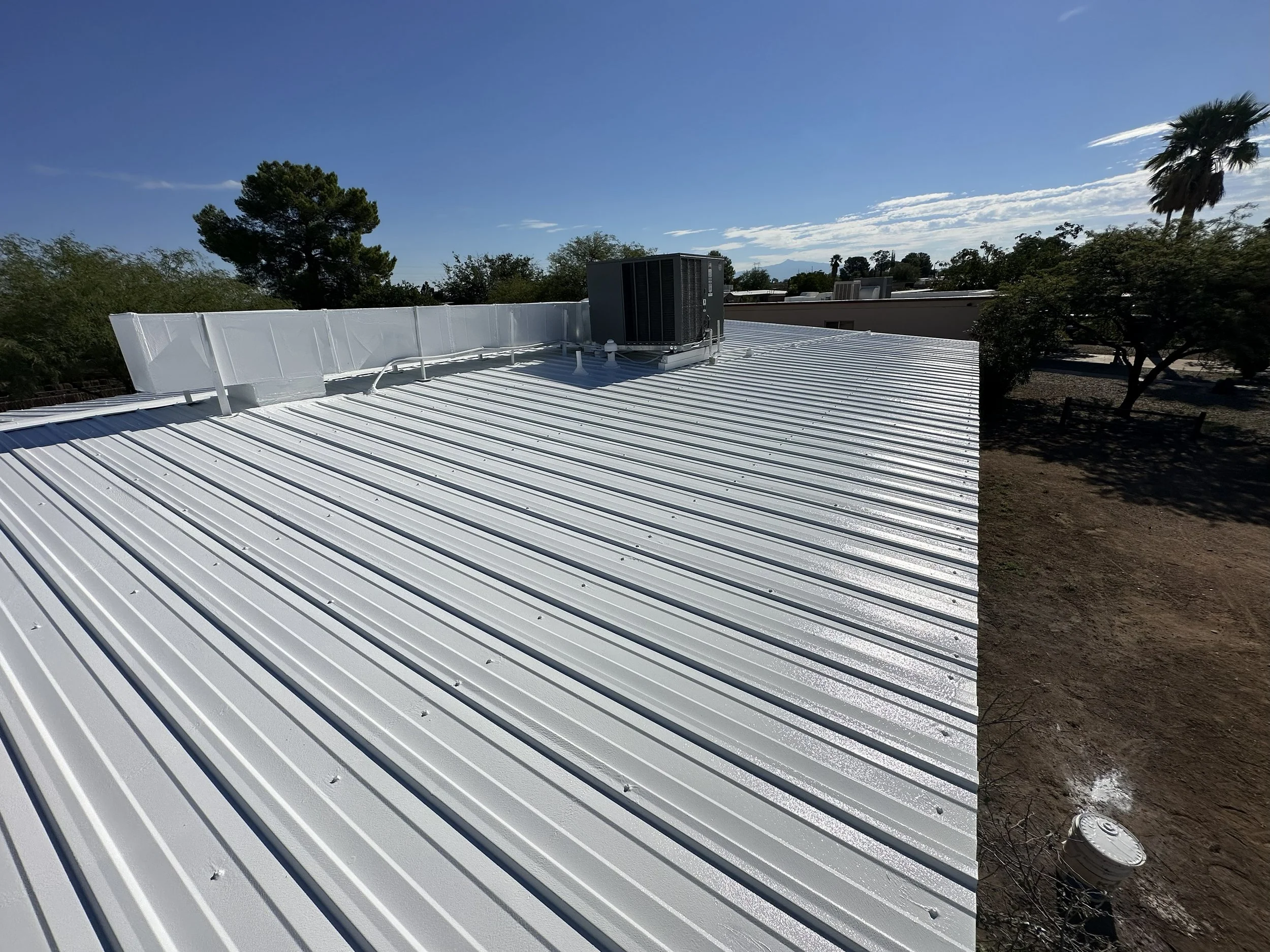 View of a corrugated metal rooftop with an HVAC unit, clear blue sky, and surrounding trees.