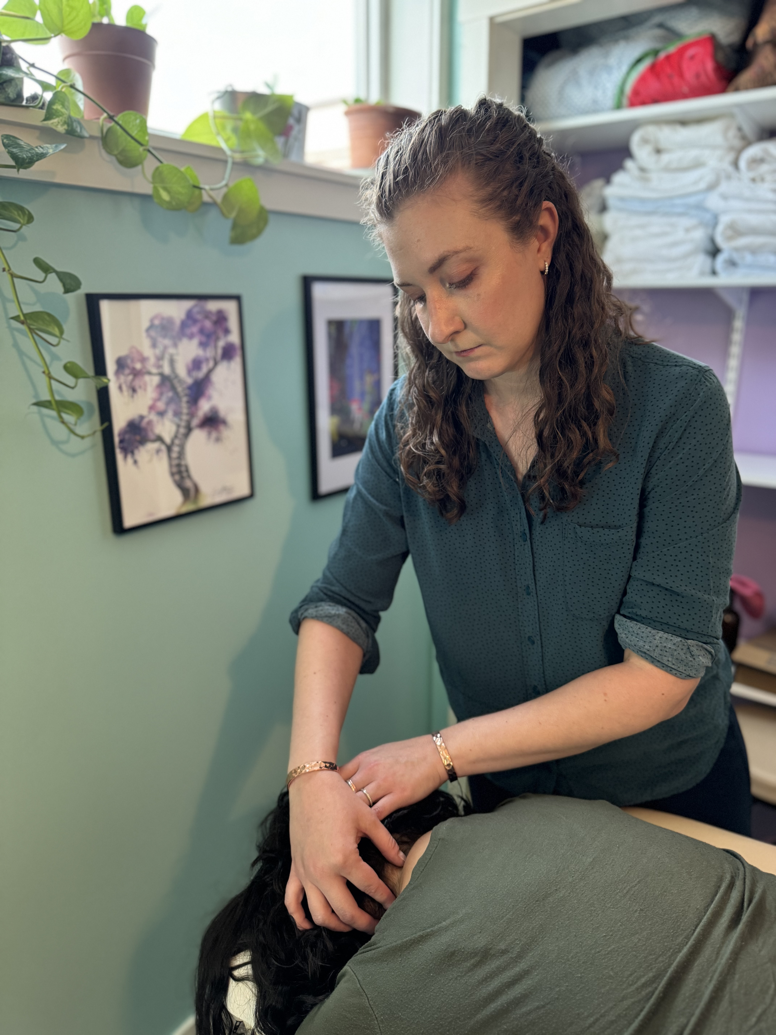 Dr. Brenna working with a client lying face down, in a room with framed artwork and shelves.