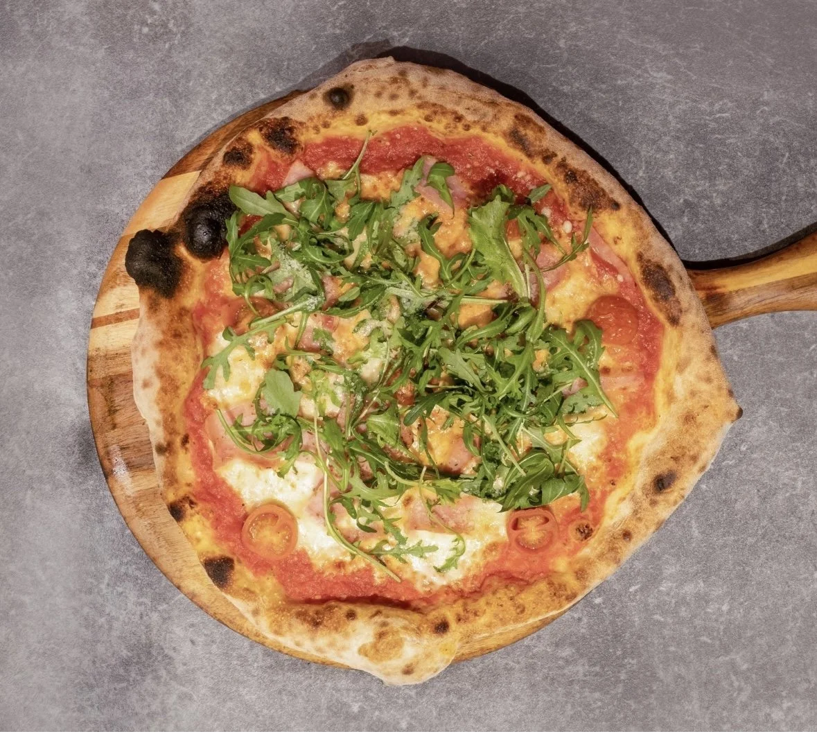 Pizza topped with cherry tomatoes, arugula, and cheese on a wooden serving board.