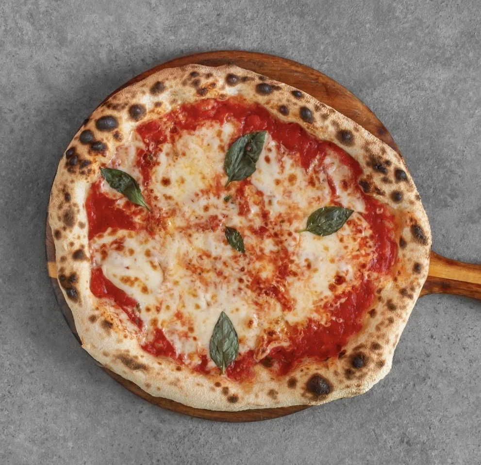 A Margherita pizza with melted cheese, tomato sauce, and fresh basil leaves on a wooden paddle.