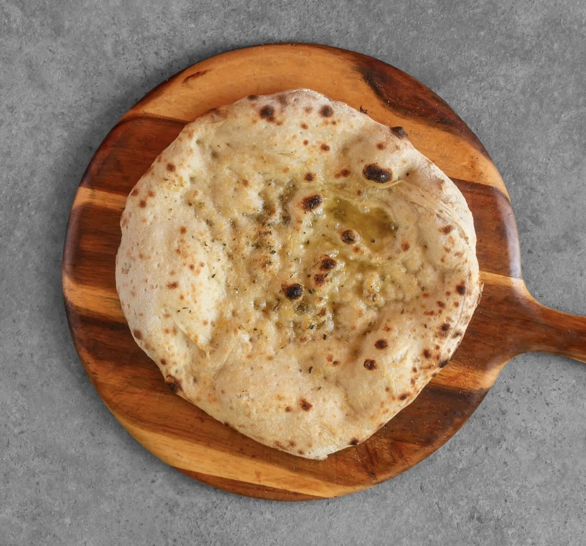 A cheese pizza with a slightly irregular round shape on a wooden serving board, placed on a gray surface.