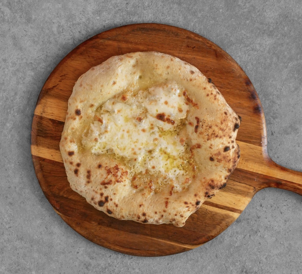 A Neapolitan-style pizza with cheese on a wooden pizza peel on a gray surface.