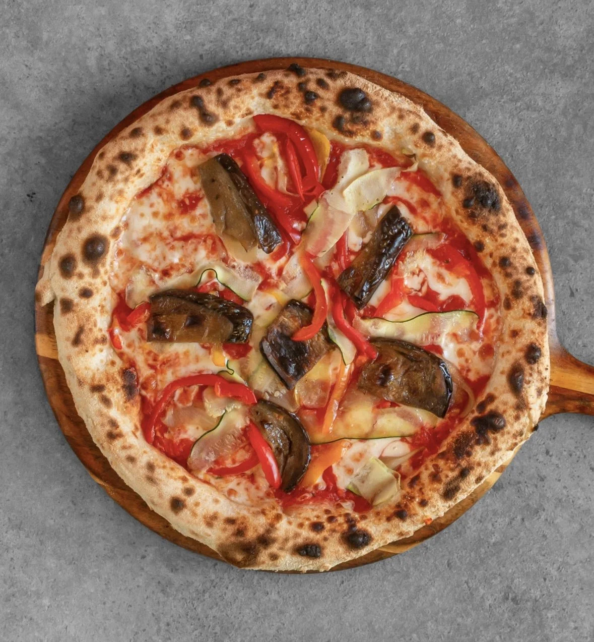 Pizza with eggplant, red bell peppers, and cheese on a wooden serving board.