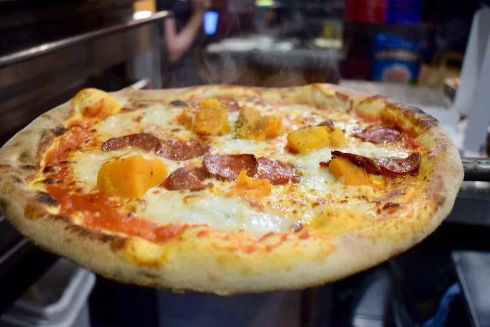 Close-up of a cheese and meat pizza with pepperoni and orange peppers, on a pizza peel.