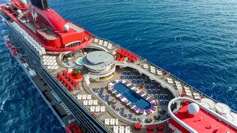Top view of a cruise ship docked at sea, featuring pools, deck chairs, and a large red structure.