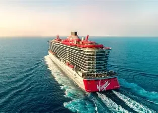 A large cruise ship sailing in open waters with a red and white exterior and the Virgin logo on the back.