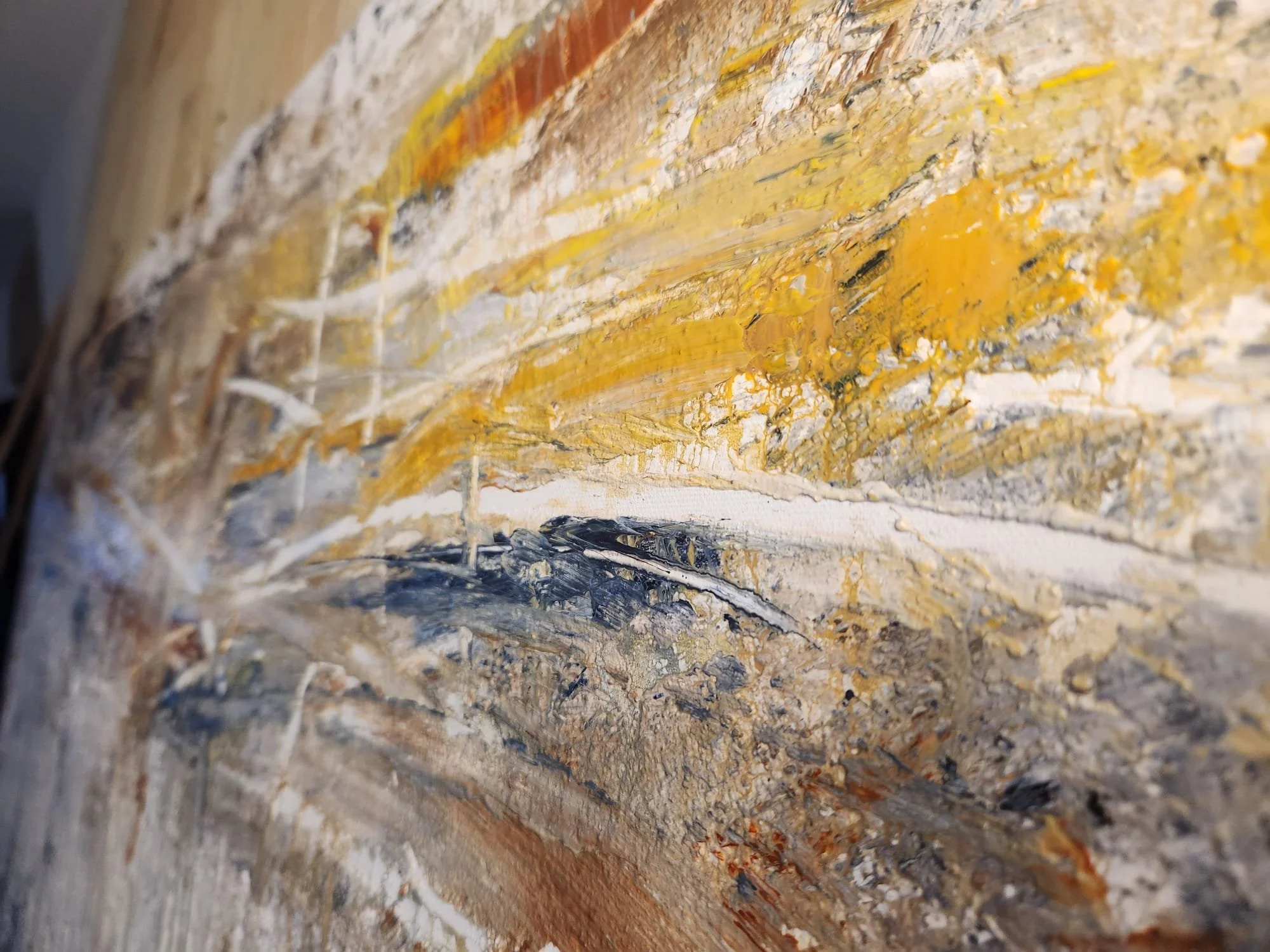 Close-up of an abstract textured painting with shades of yellow, white, and gray on a wooden surface.