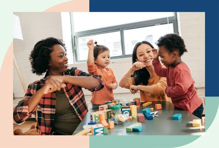 Two women and two young girls playing with colorful alphabet blocks at a table, smiling and engaging with each other.