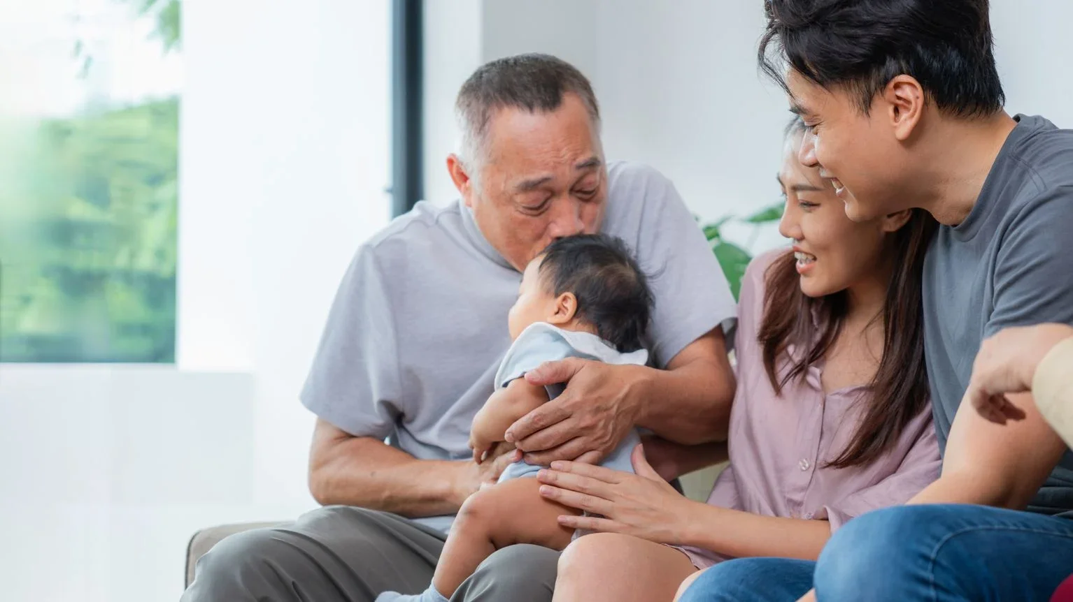 Family joyfully holding and kissing a young child in a bright living room.