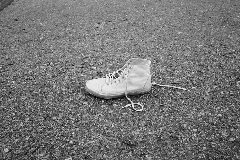 A white sneaker lies on a gravel road, with the laces loosely tied and left untied.