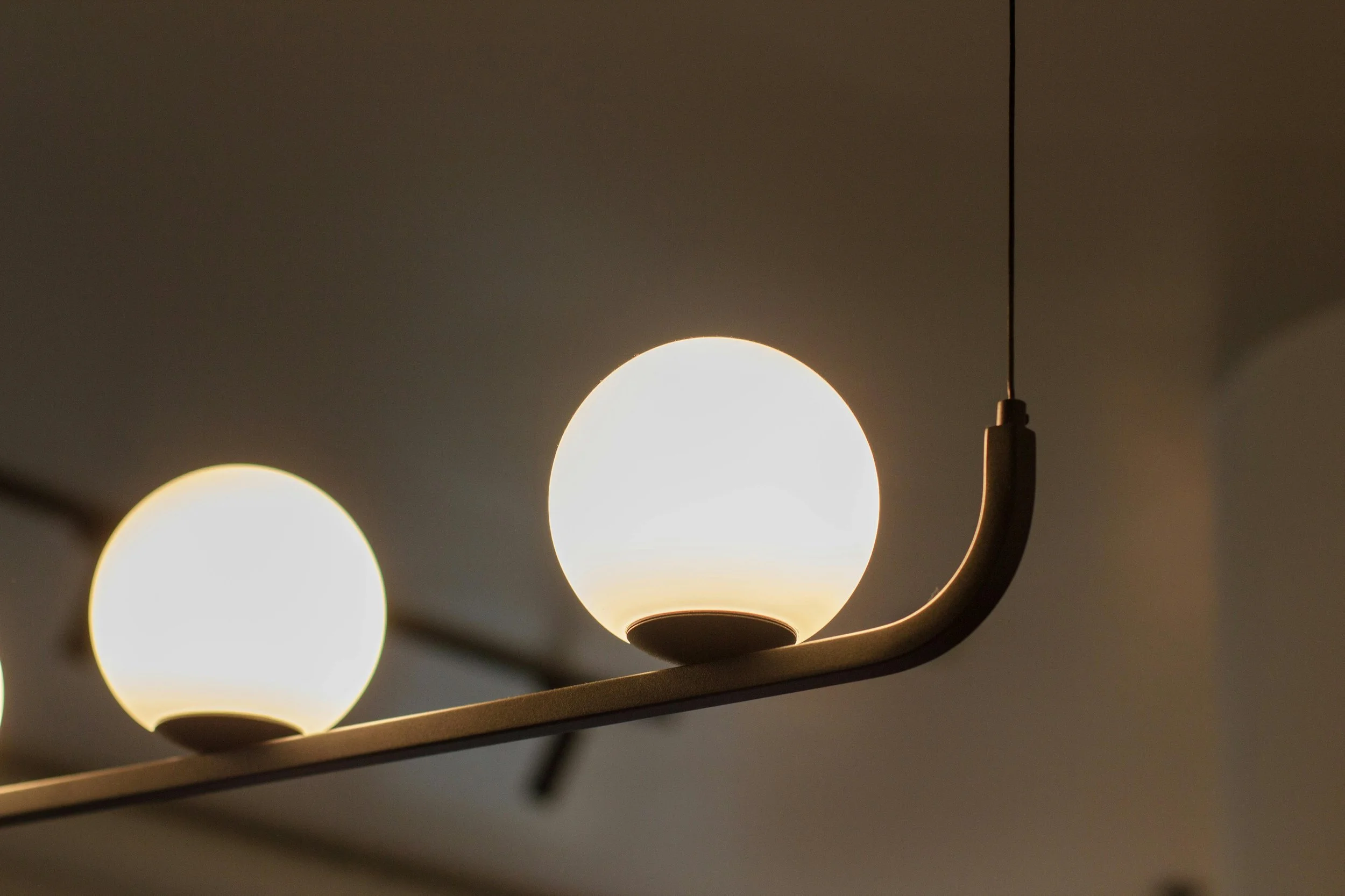 Close-up of a ceiling light fixture with three spherical white bulbs against a dark ceiling.
