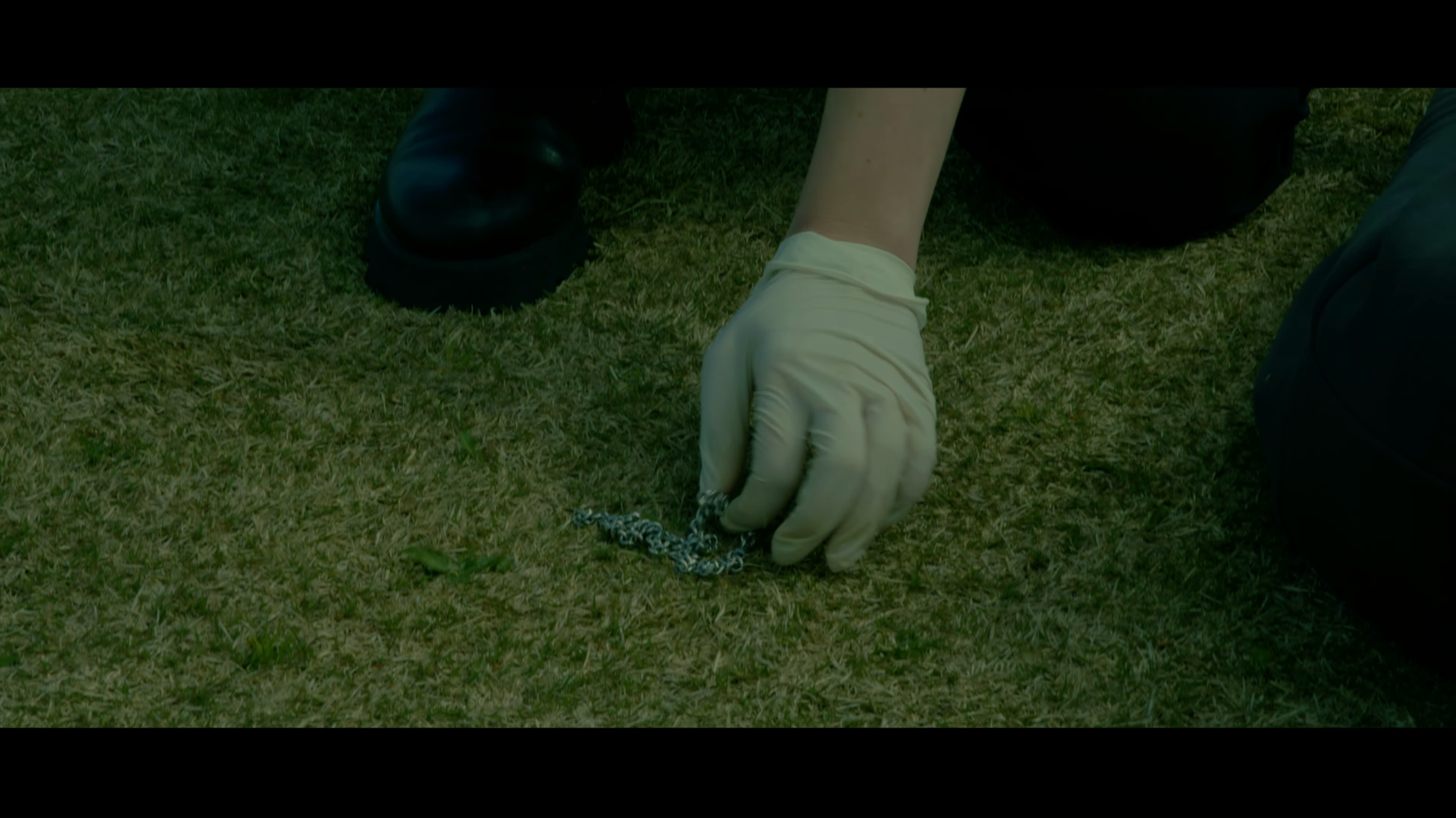 Person wearing a beige glove and dark clothing picks up a chain on grass.