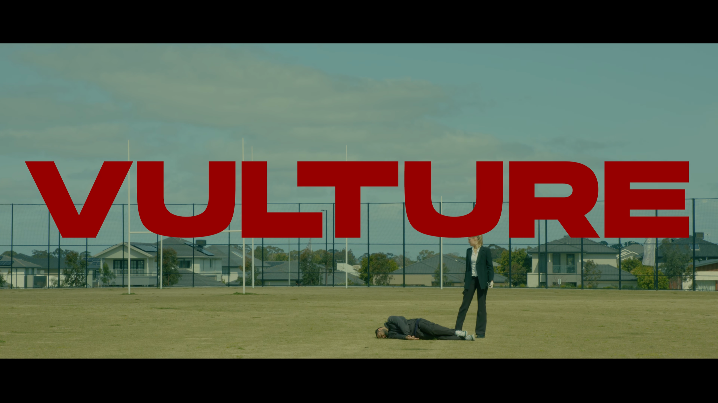 A scene from a sports field with two people, one lying on the ground and the other standing nearby, overlaid with the word 'VULTURE' in large red letters.