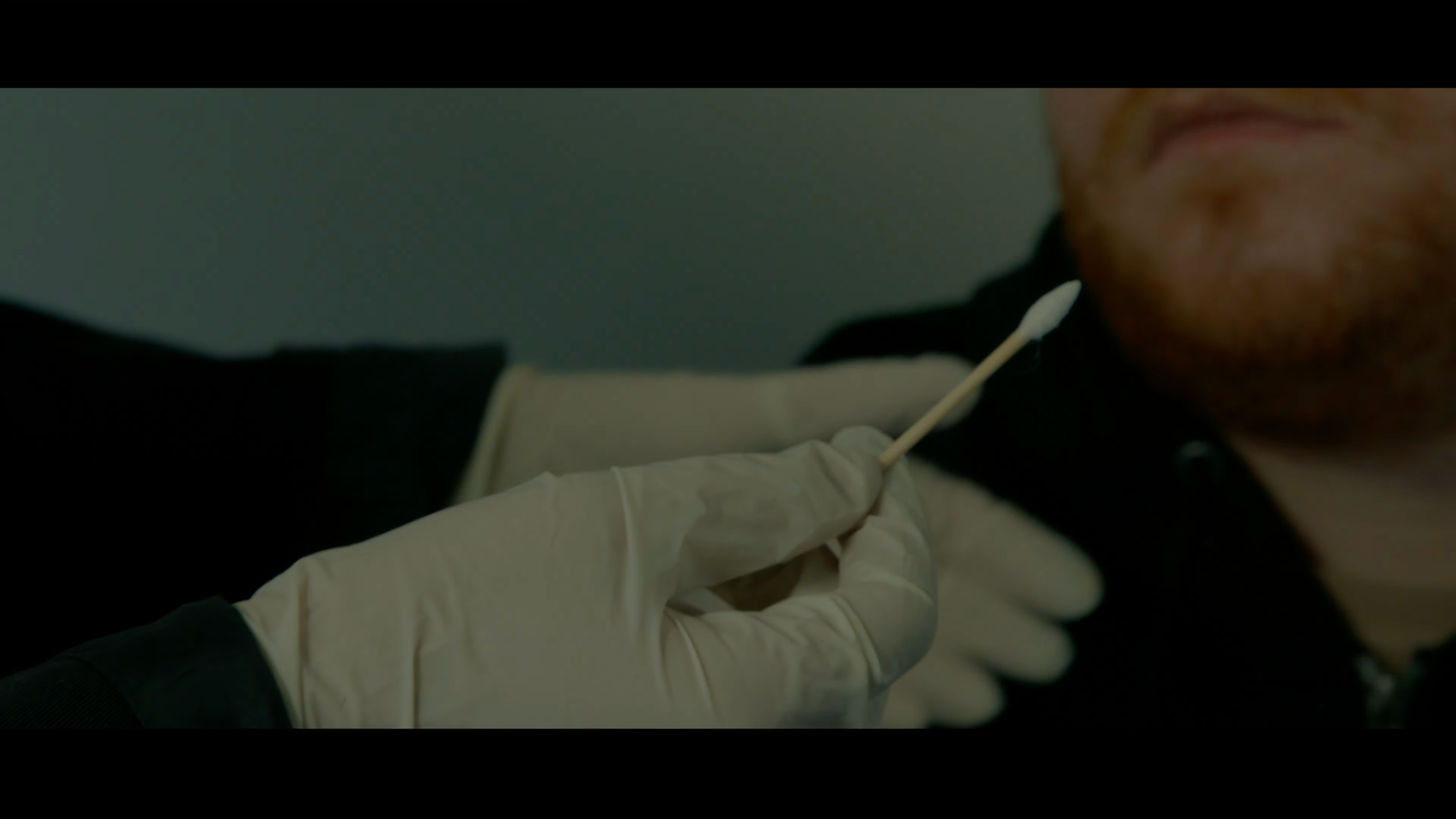 A person wearing gloves is administering a nasal test using a swab to another person in a close-up shot.