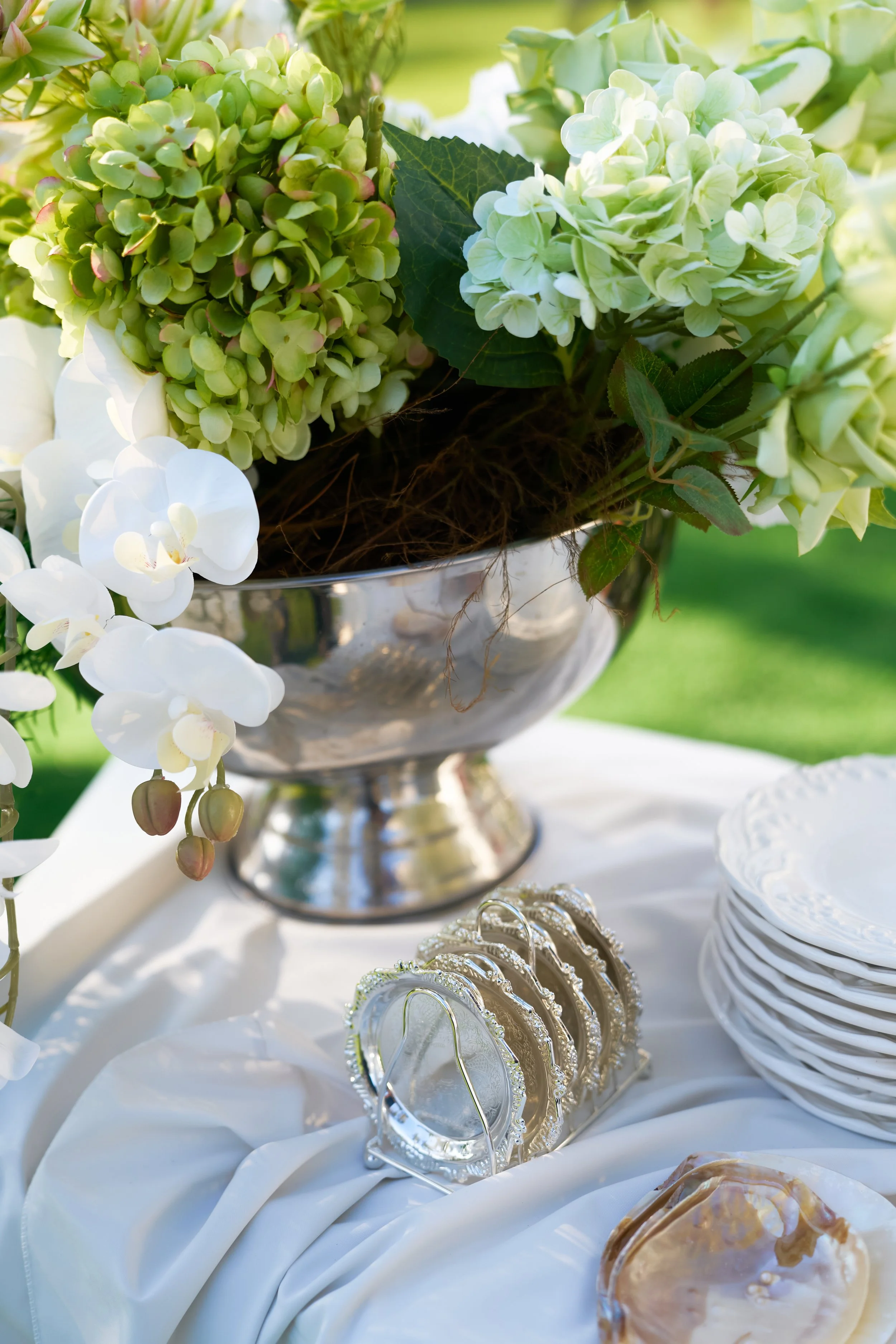 Luxury wedding table styling with green hydrangea centrepiece in champagne cooler, elegant snack plates, European-style plates and white linen draping by Rumi Hires