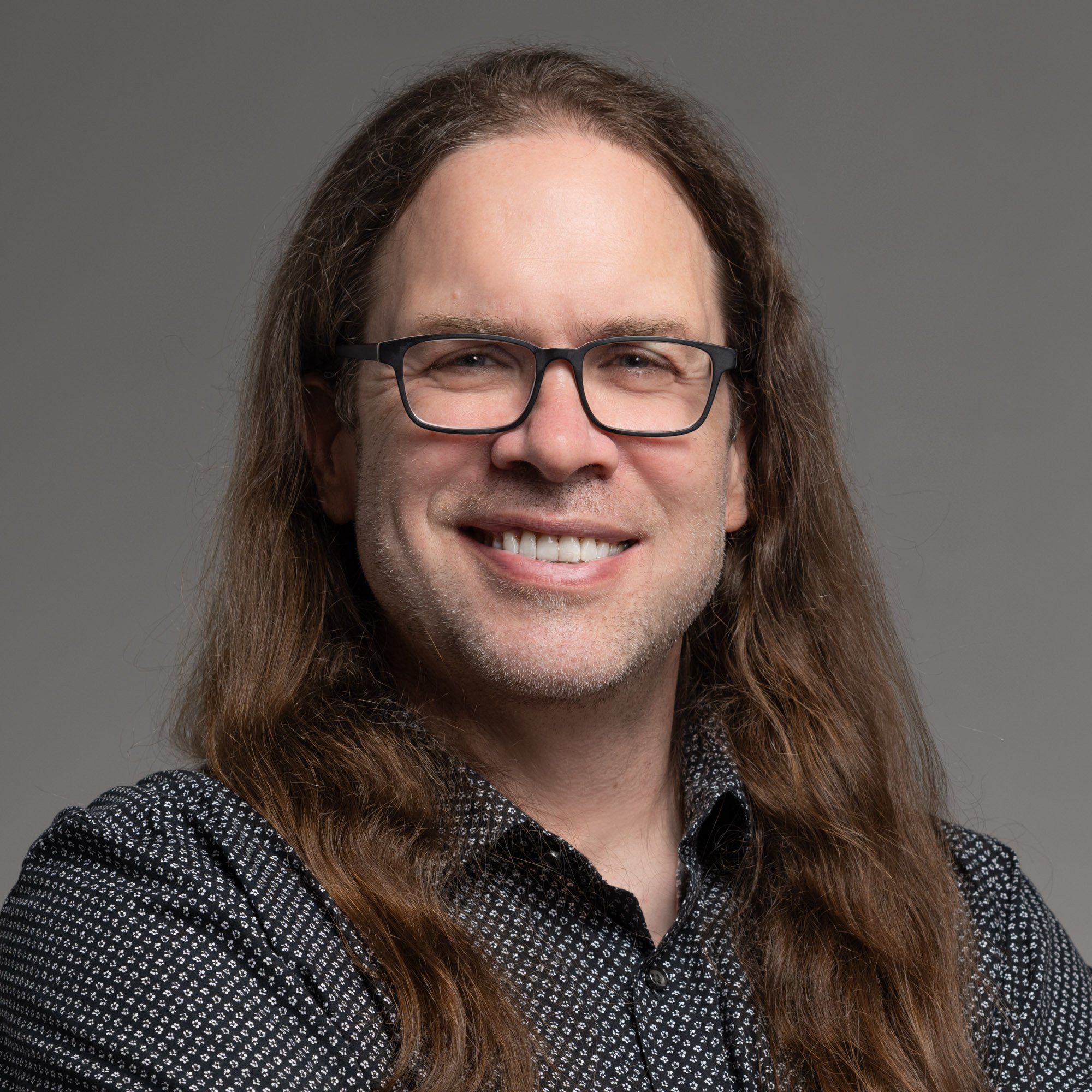 Black and white portrait of a man smiling and looking to the right, wearing a dark collared shirt.