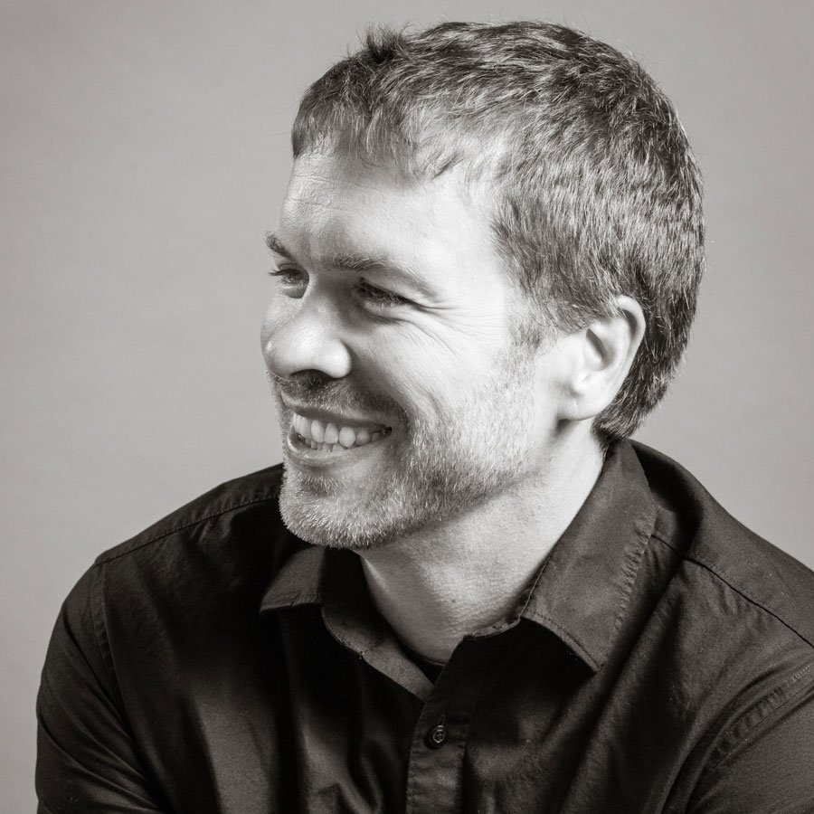 Black and white portrait of a man smiling and looking to the right, wearing a dark collared shirt.
