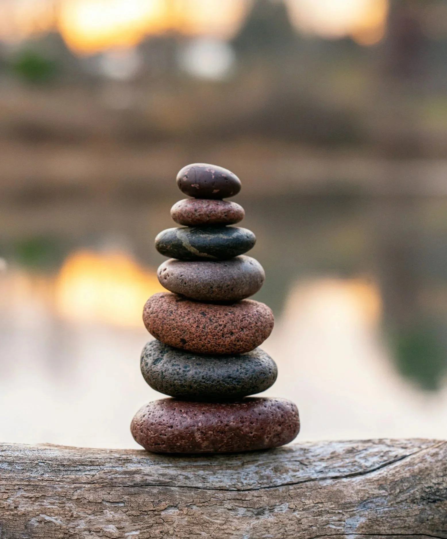 Stacked smooth stones balanced on a piece of driftwood during sunset.