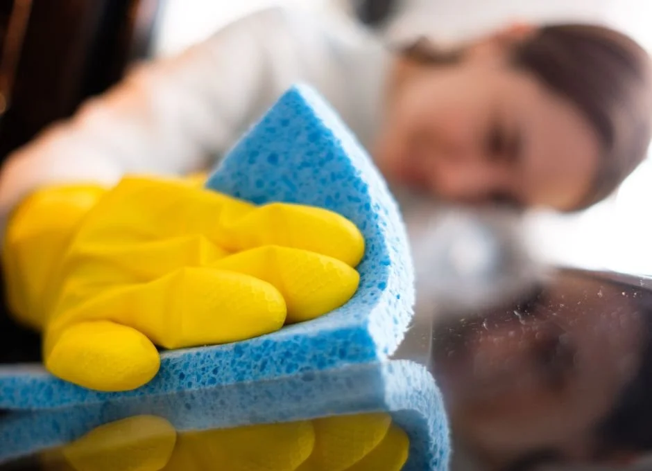 Person cleaning a reflective surface with a blue sponge and yellow glove.