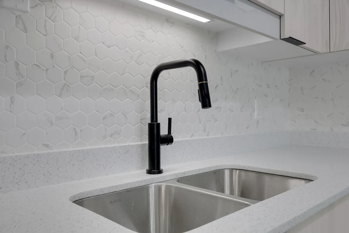 Close-up of a modern kitchen renovation in Calgary showcasing quartz countertops, a stainless steel undermount sink, matte black pull-down faucet, and marble-look hexagon tile backsplash completed by Da Vinci Contracting.