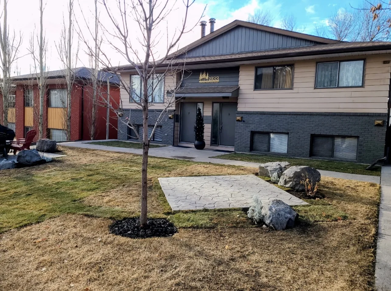 Finished front yard landscaping featuring a stamped concrete patio, natural stone accents, and refreshed lawn for a residential property in Calgary.