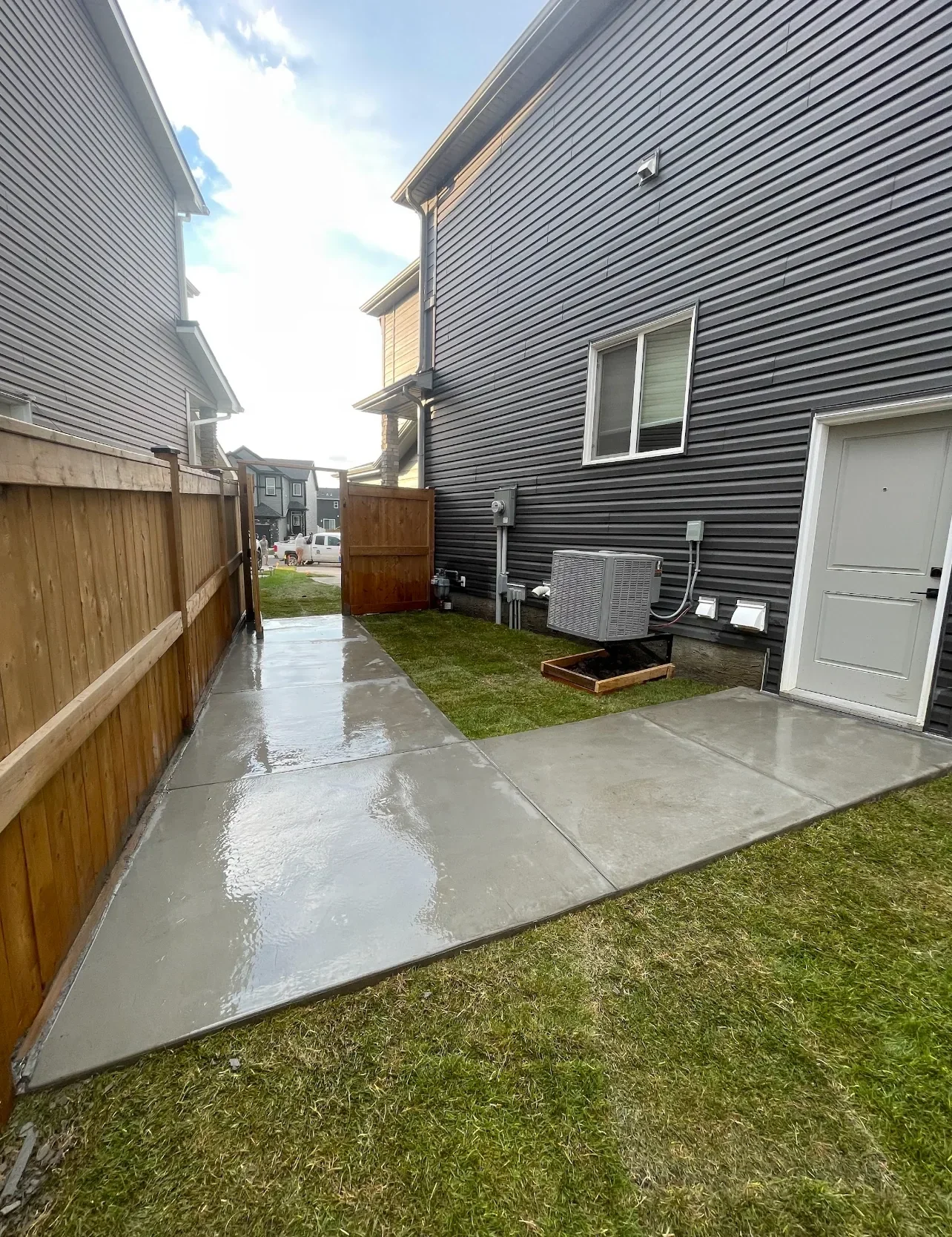Completed backyard landscaping featuring a freshly poured concrete walkway, clean grading, and new sod installation for a residential home in Calgary.