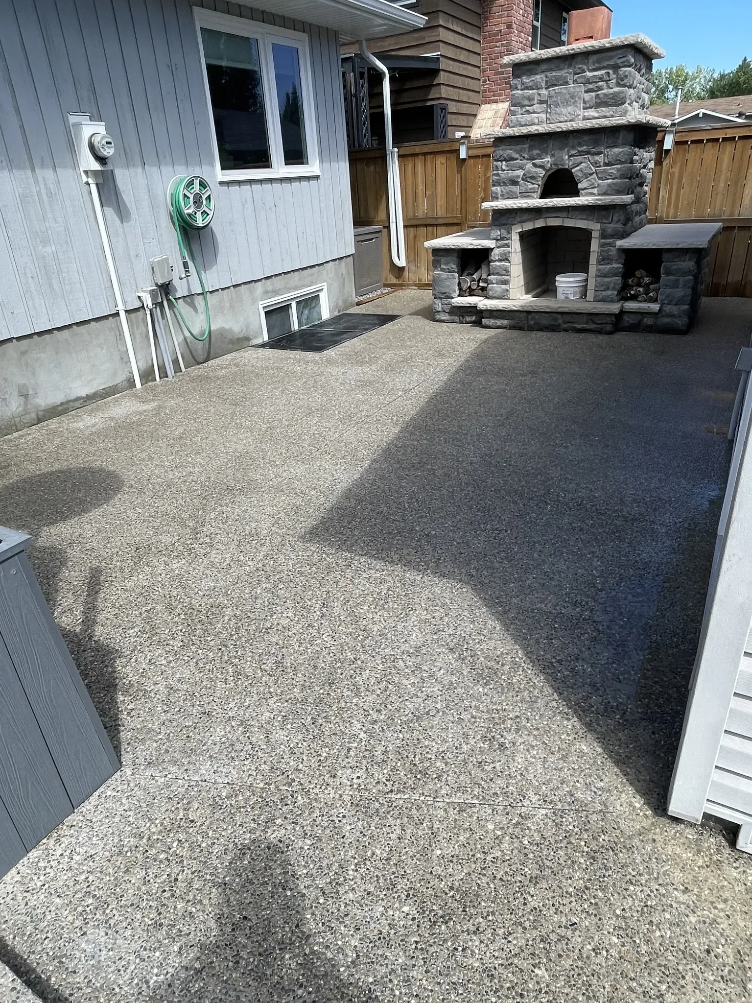 Exposed aggregate concrete patio finished with clean control joints, creating a durable, slip-resistant outdoor living space centered around a custom stone fireplace.