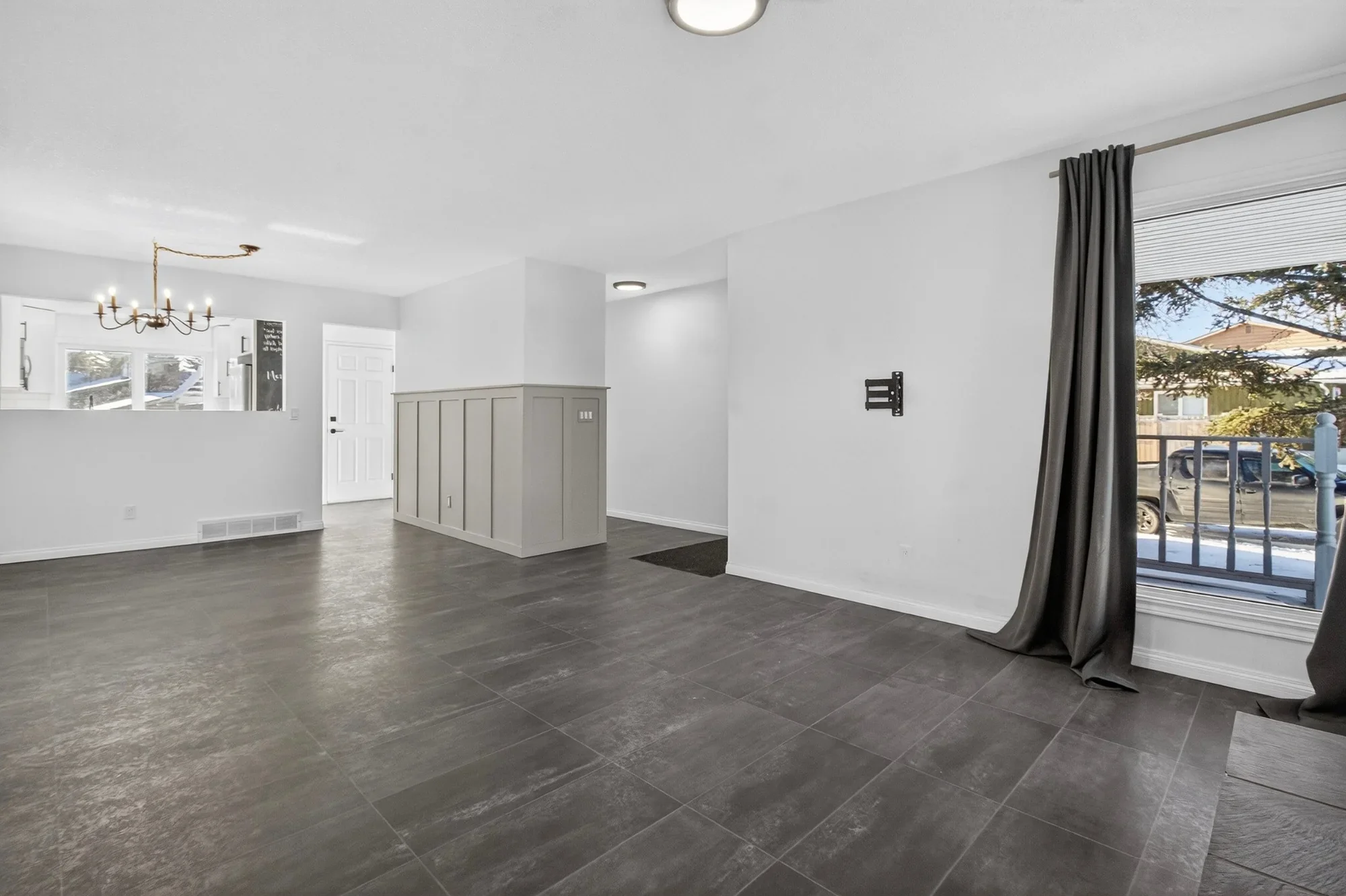 Open-concept living room renovation featuring large-format tile flooring, fresh neutral paint, custom wainscoting detail, updated lighting, and modern finishes.