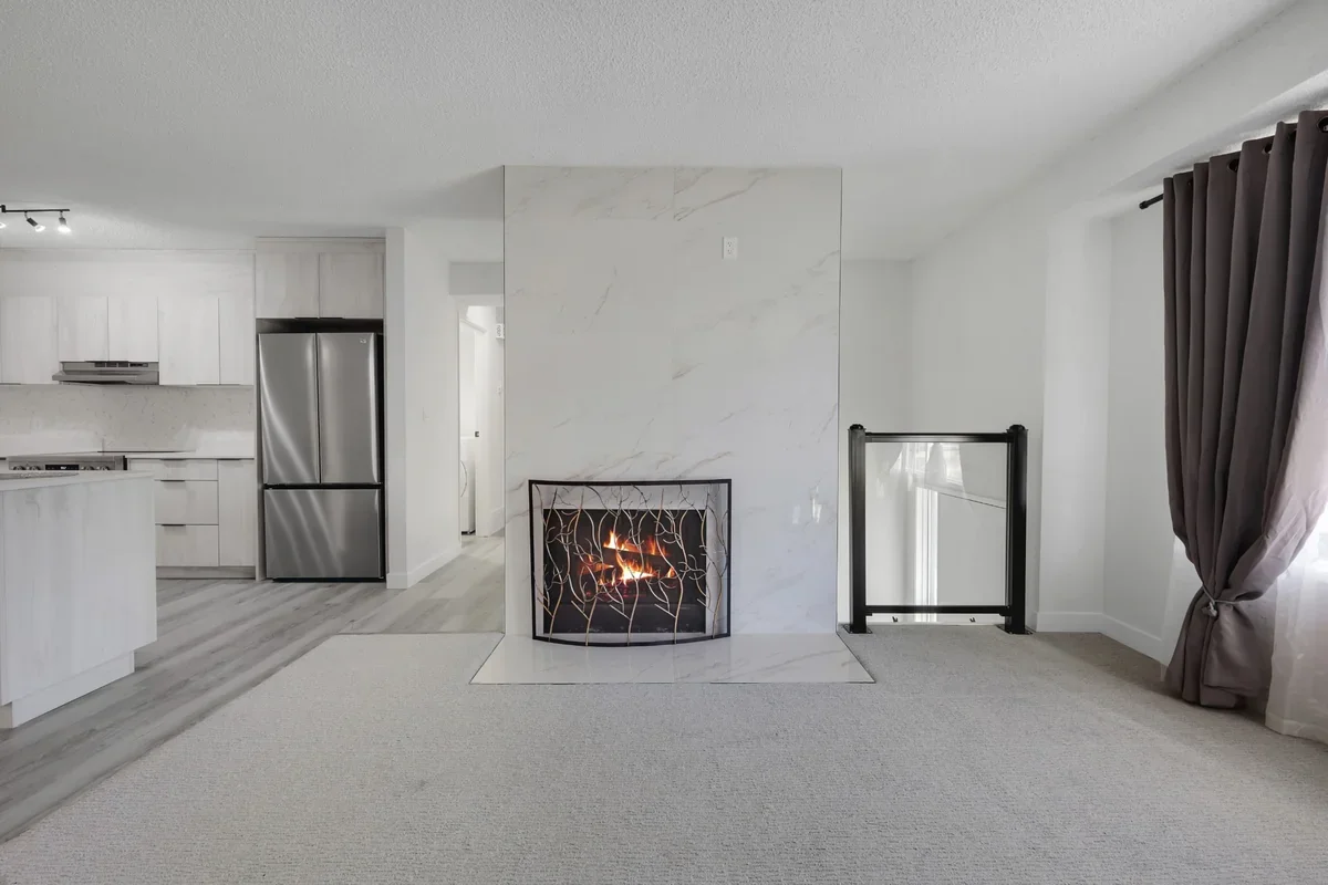 Bright open-concept living room renovation featuring a floor-to-ceiling marble fireplace, modern kitchen with stainless steel appliances, new flooring, and premium finishes completed by Da Vinci Contracting in Calgary.