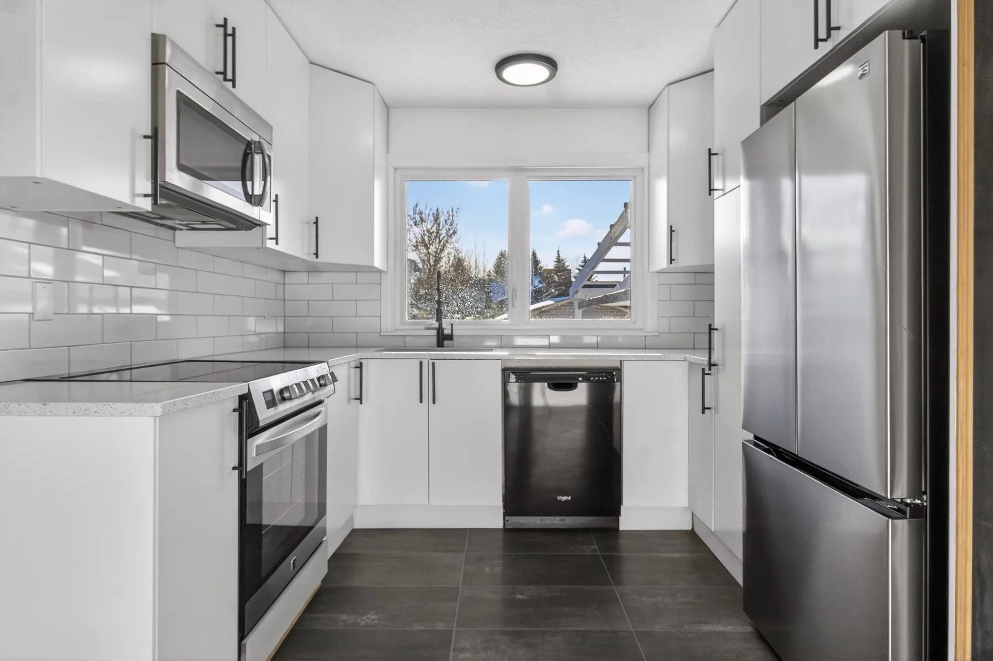 Bright modern kitchen renovation featuring white shaker-style cabinets, subway tile backsplash, stainless steel appliances, quartz countertops, and large-format tile flooring.
